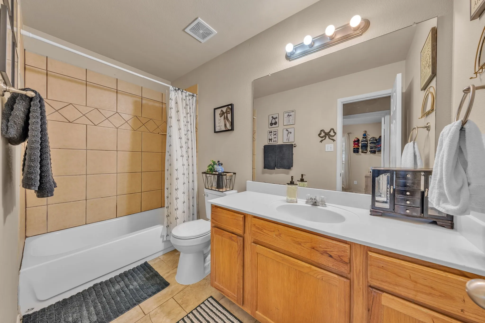 Full bathroom featuring a single vanity with wood cabinetry and a white countertop, a shower-tub combination with tiled surround, and tile flooring