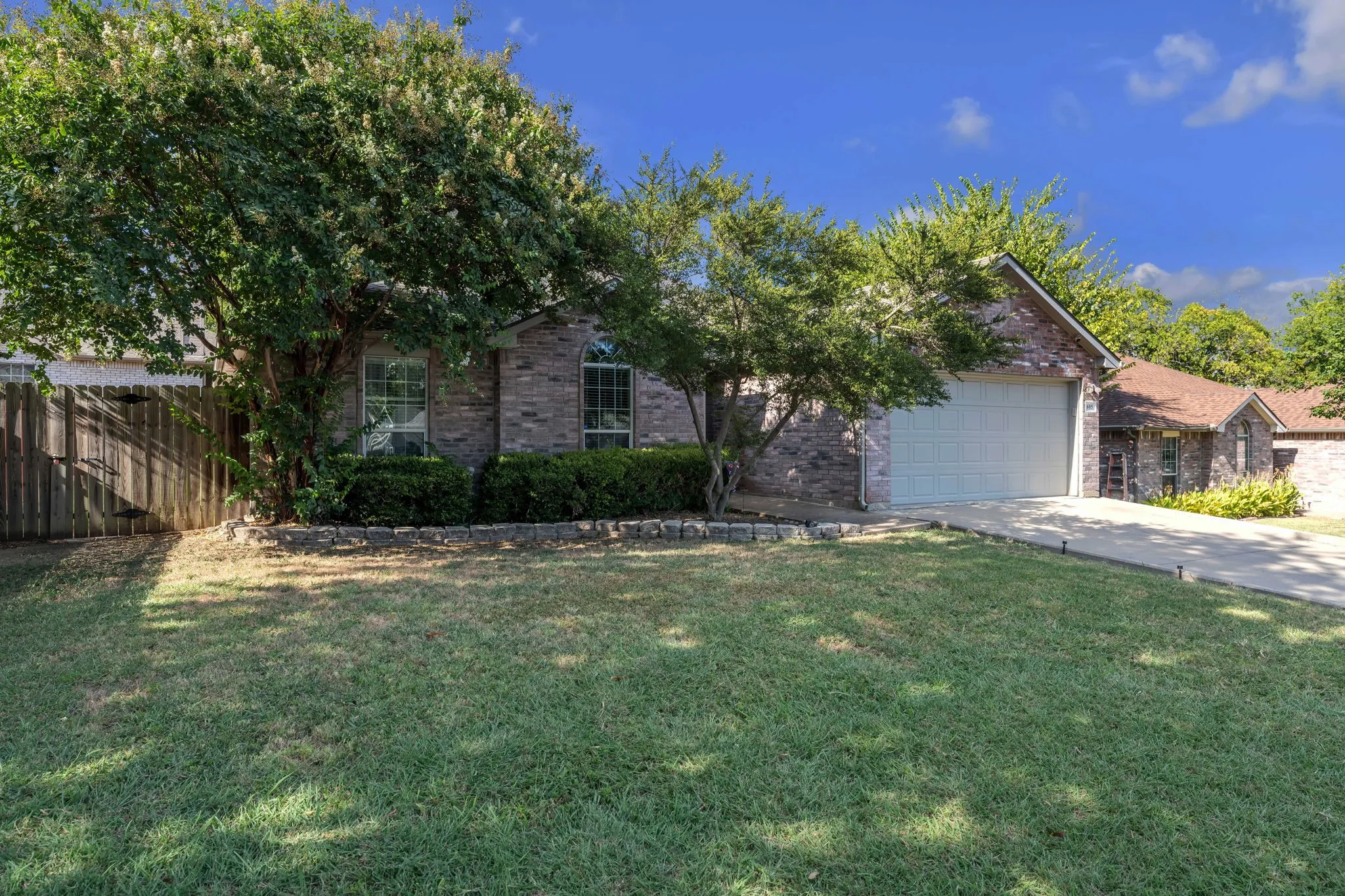 Brick exterior, arched windows, attached garage, concrete driveway, and mature landscaping