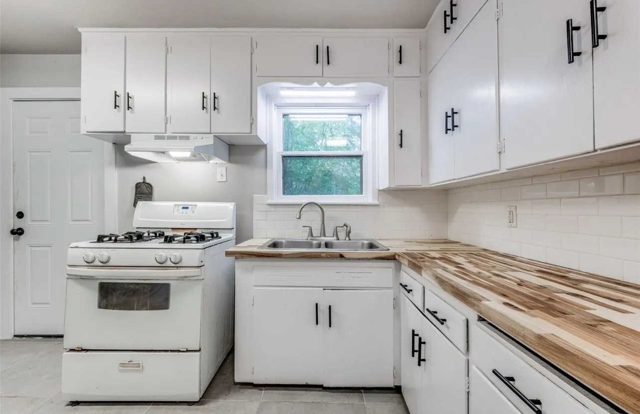 White cabinetry with matte black hardware, butcher block countertops, white subway tile backsplash, and a stainless steel sink with a gooseneck faucet