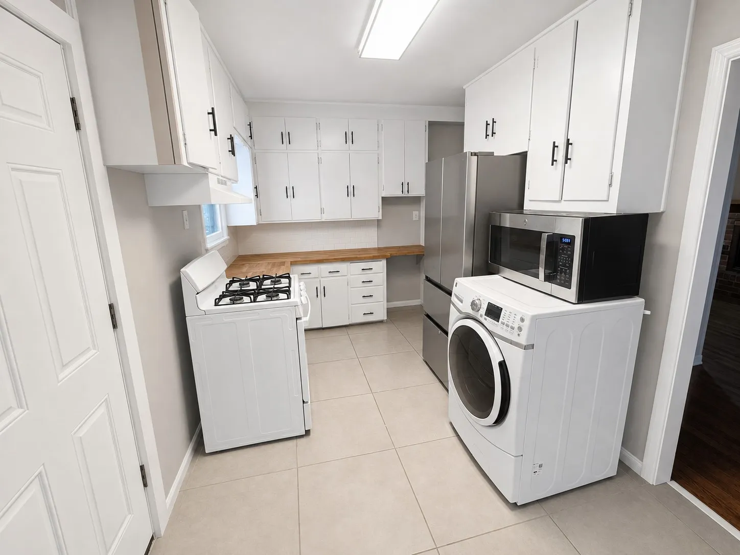 Kitchen featuring white cabinetry, light wood-finish countertops, tiled flooring, a gas range, and a stainless steel refrigerator