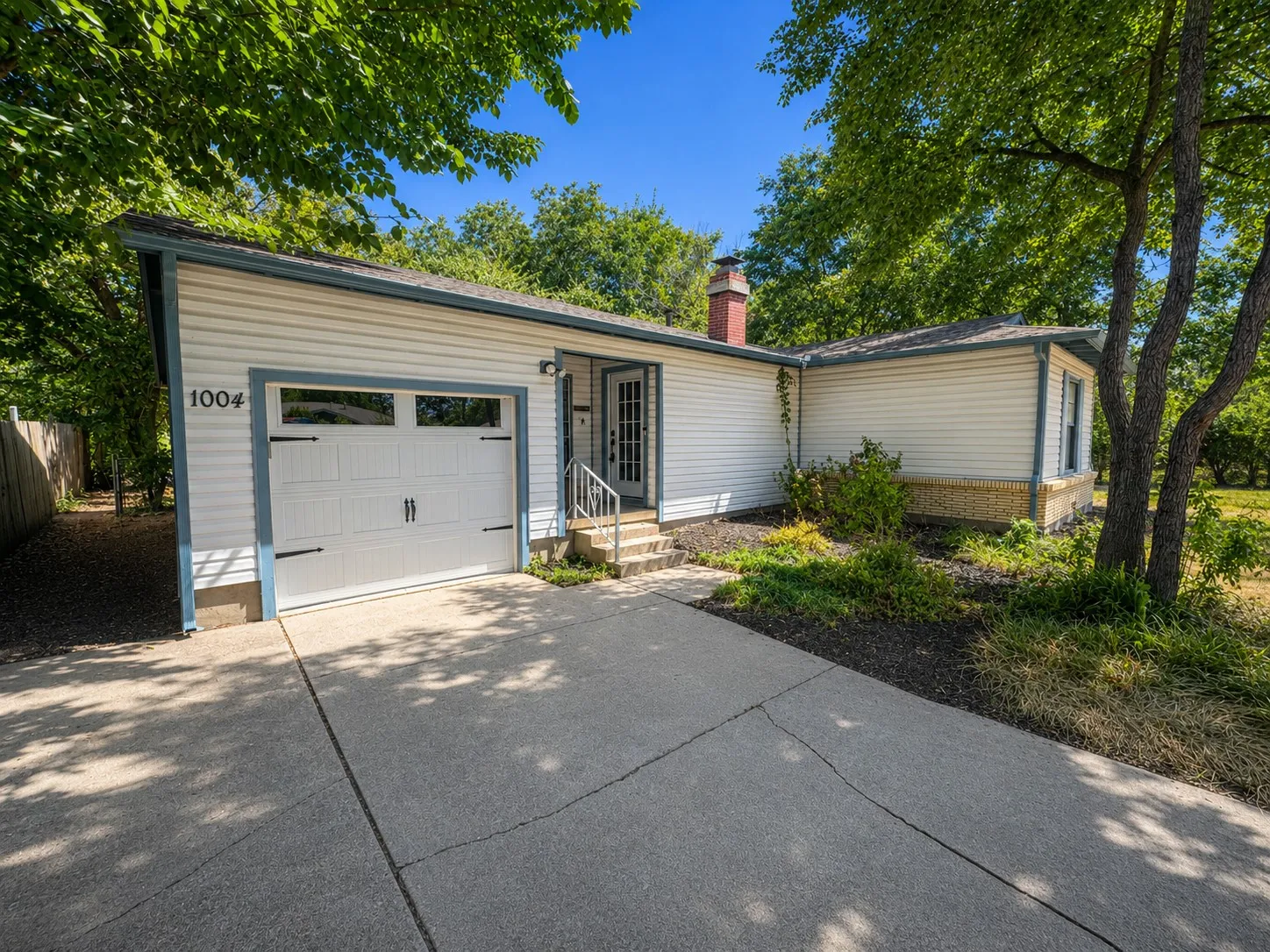 White siding exterior with a single-car garage, concrete driveway, and mature landscaping