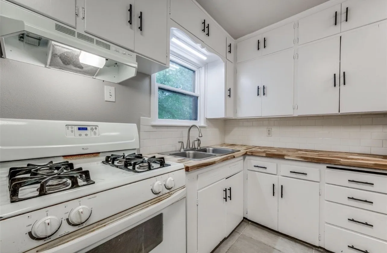 Bright, updated kitchen featuring white cabinetry with hardware accents, wood-finish countertops, a professional-style gas cooktop, stainless steel sink with chrome faucet, and natural light from a window above the counter