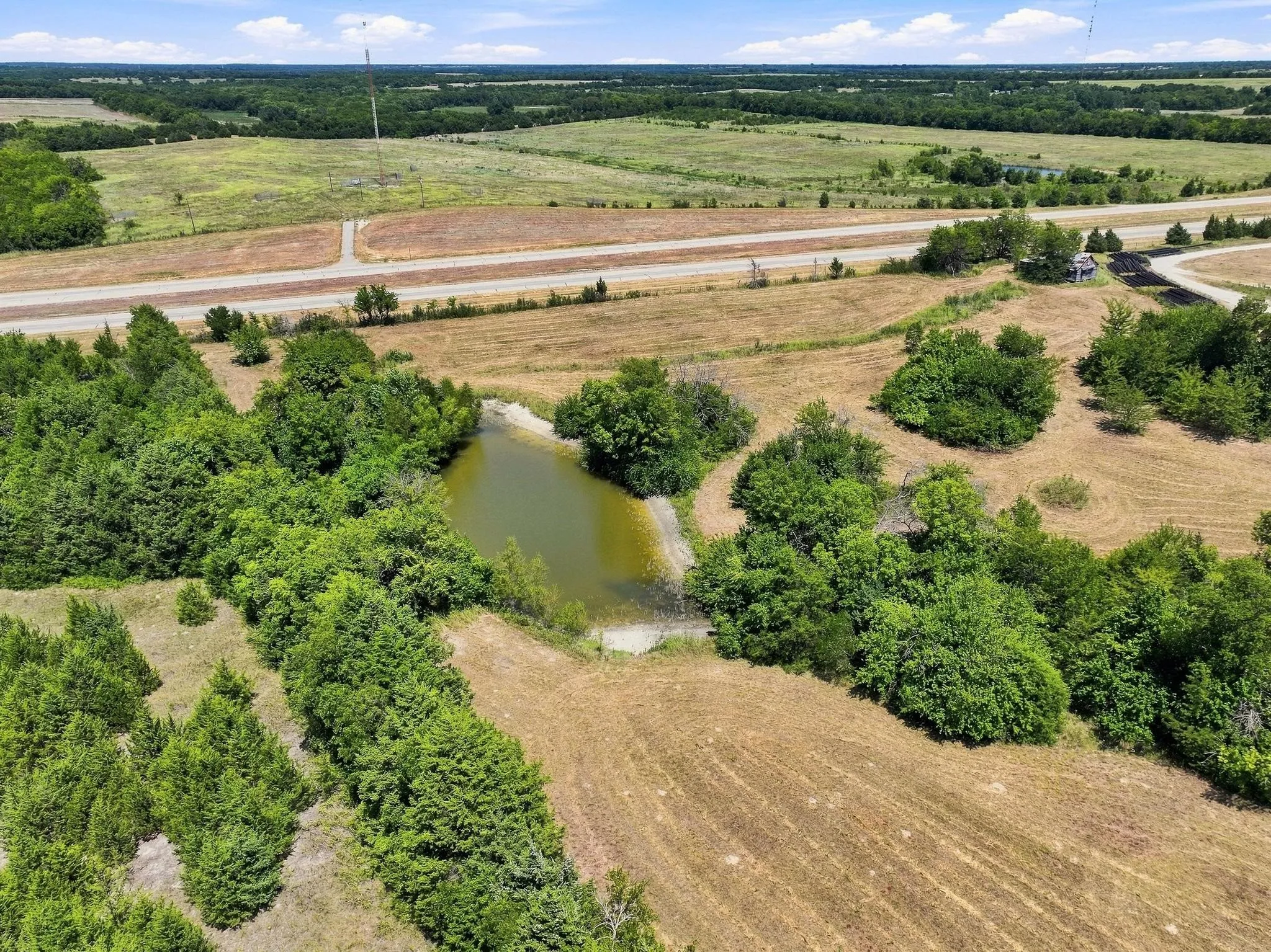 Expansive land featuring a natural pond, mature trees, and surrounding open fields