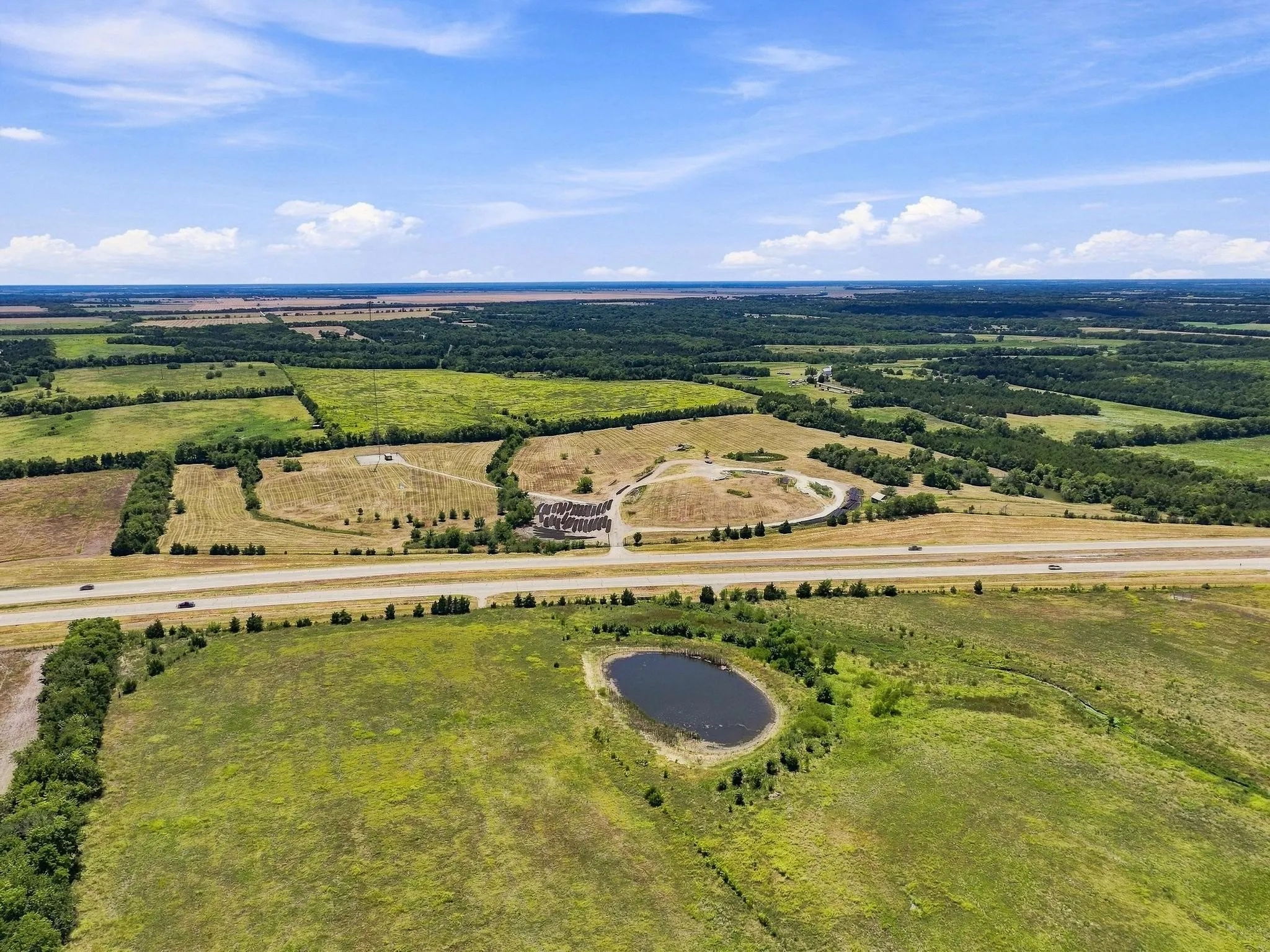 Expansive rural landscape featuring a pond, open fields, and a highway