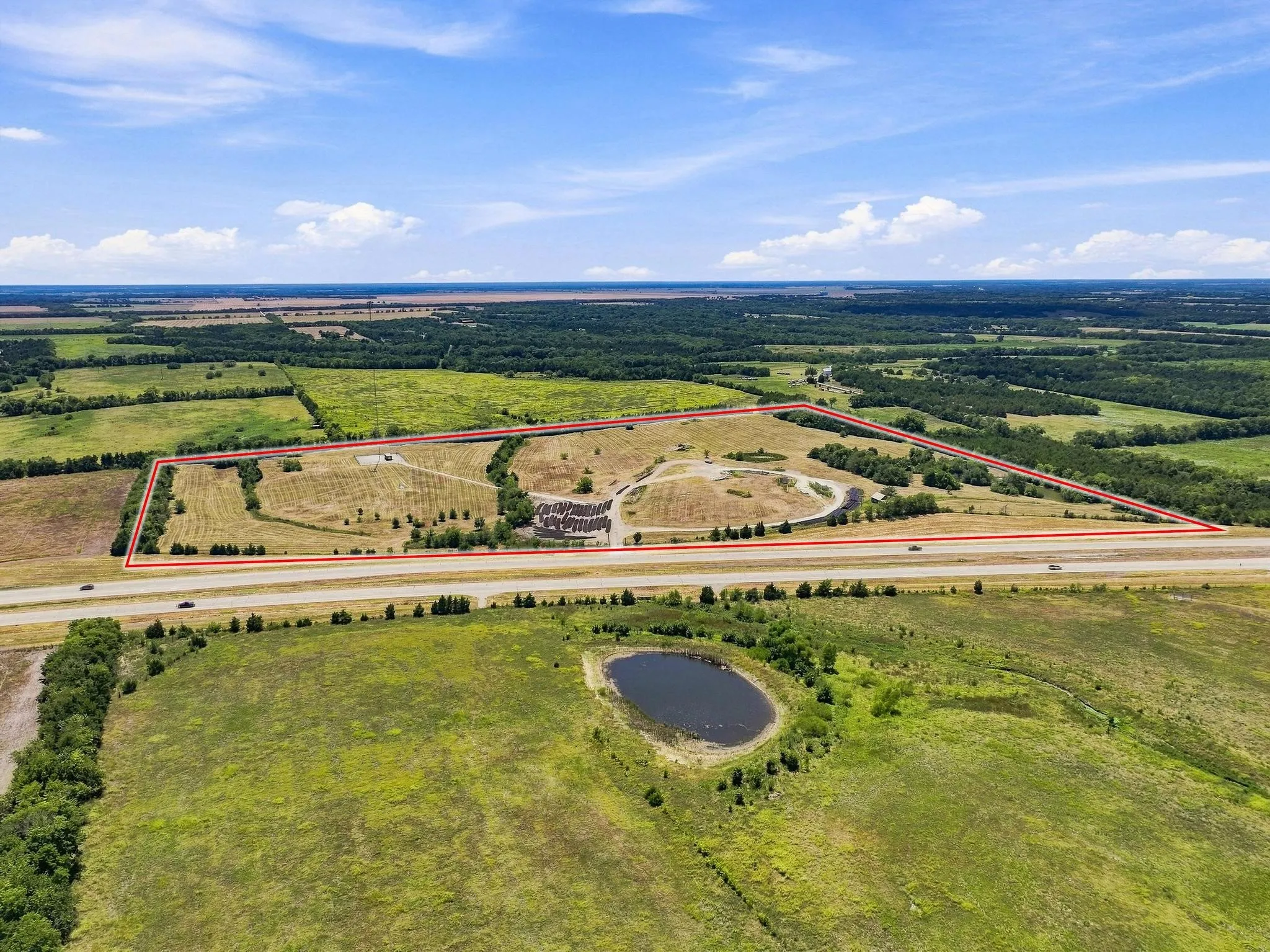 Expansive land parcel with highway frontage, surrounding open fields, and a small pond