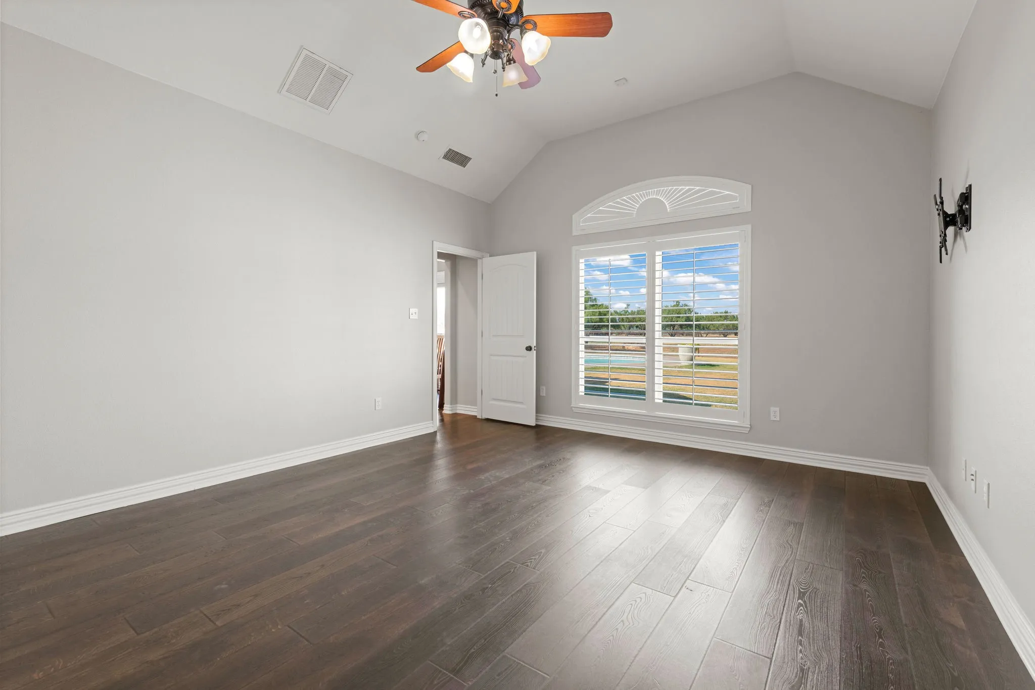Vaulted ceiling with a ceiling fan, wood-finish LVP flooring, and a double window with wood plank shutters overlooking the back yard and pool.