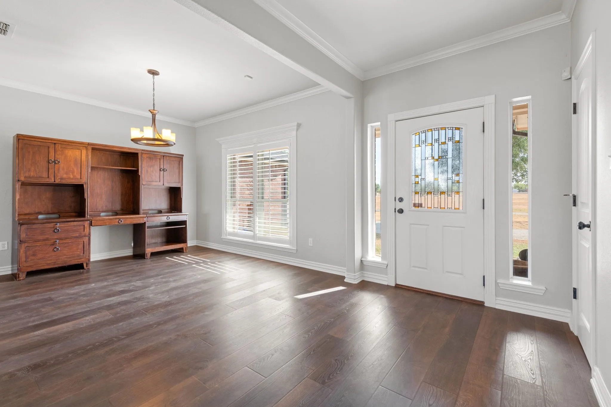 Wood-finish LVP flooring, crown molding, white trim, decorative lighting, and a front entry door with decorative glass and side lights. Wood plank shutters.