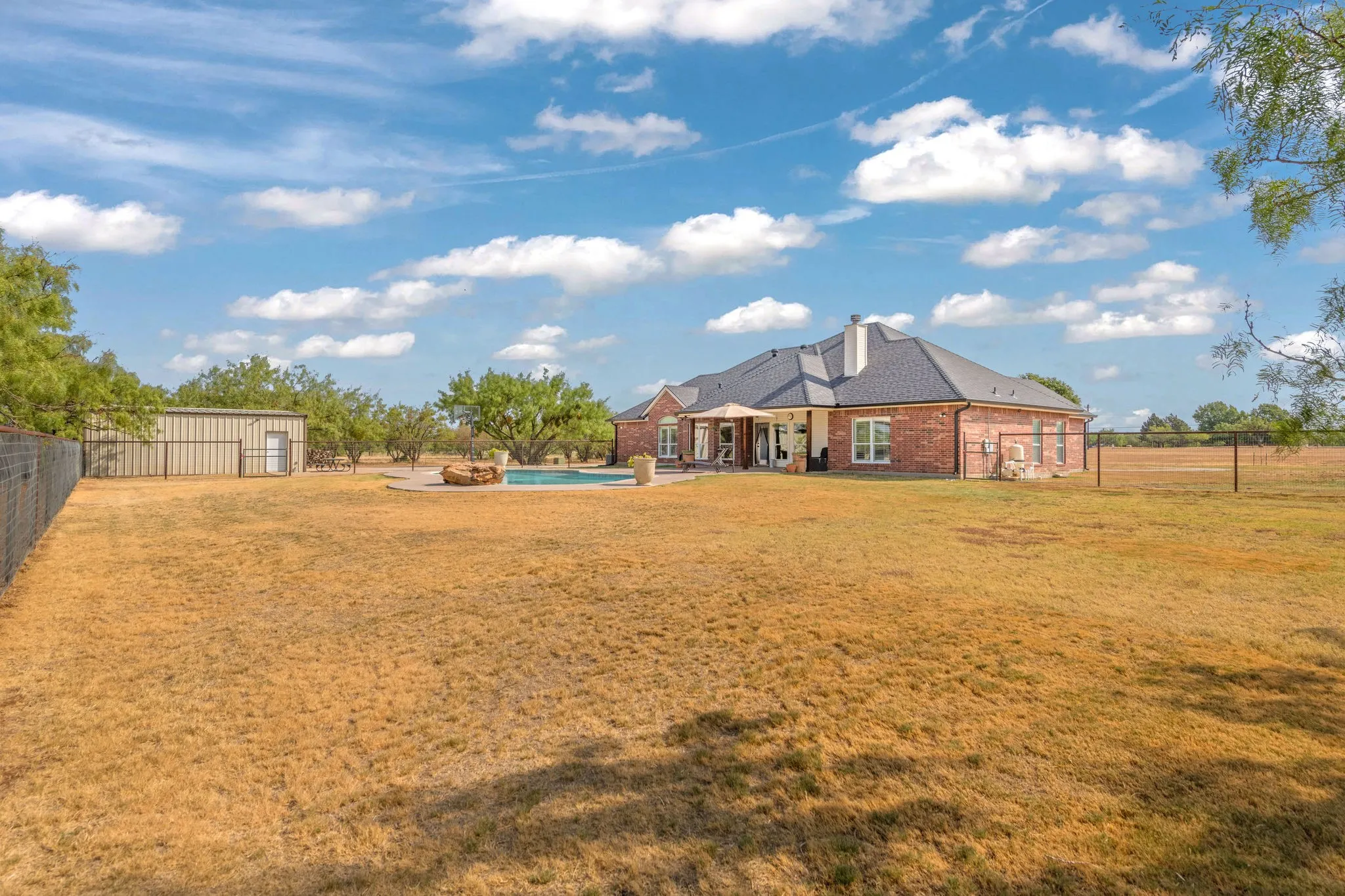 Red brick exterior with dark shingle roof, gutters, pool, and workshop.  Large fenced back yard.