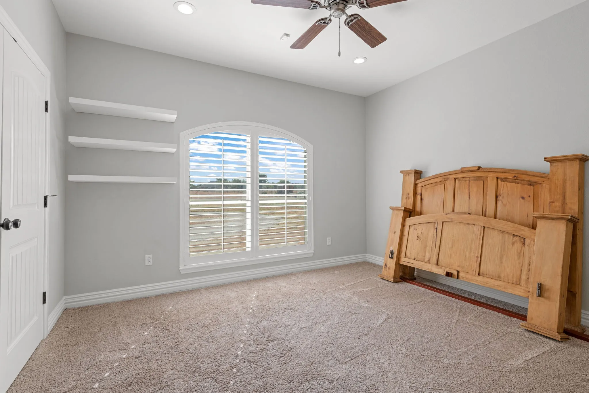 Arch-top window with wood plank shutters overlooking front yard. Recessed lighting, ceiling fan, and light-toned carpeting.  Free floating shelves.