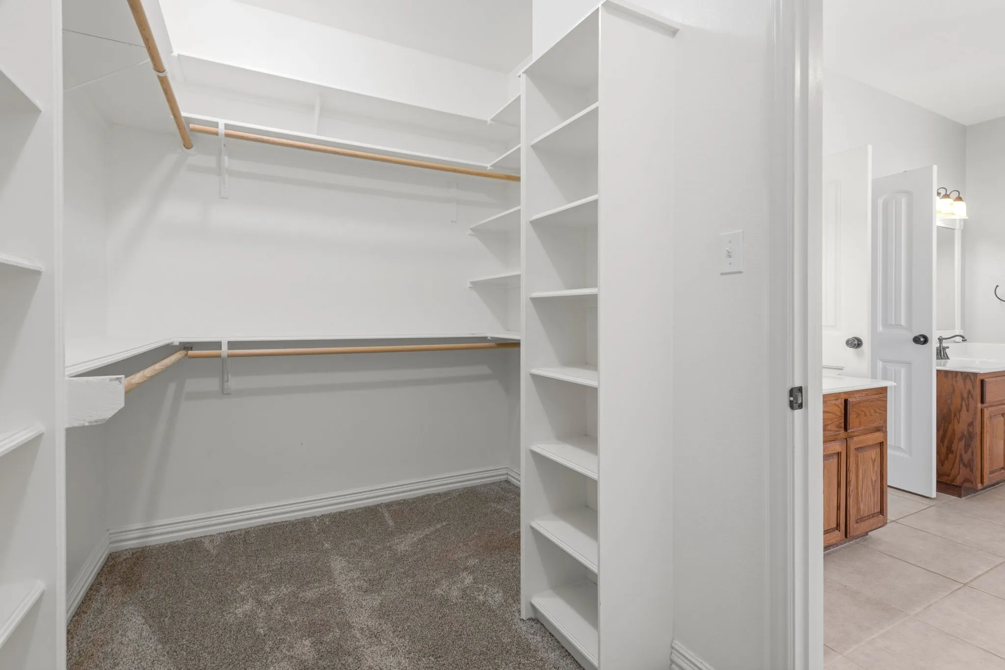 One of two walk-in closets featuring built-in shelving, multiple hanging rods, and carpet flooring.