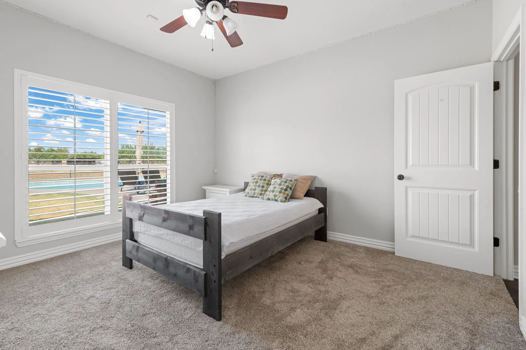 Plush carpet flooring, light wall tones, white trim, and a ceiling fan with light fixture.  Nice view of back yard and pool.