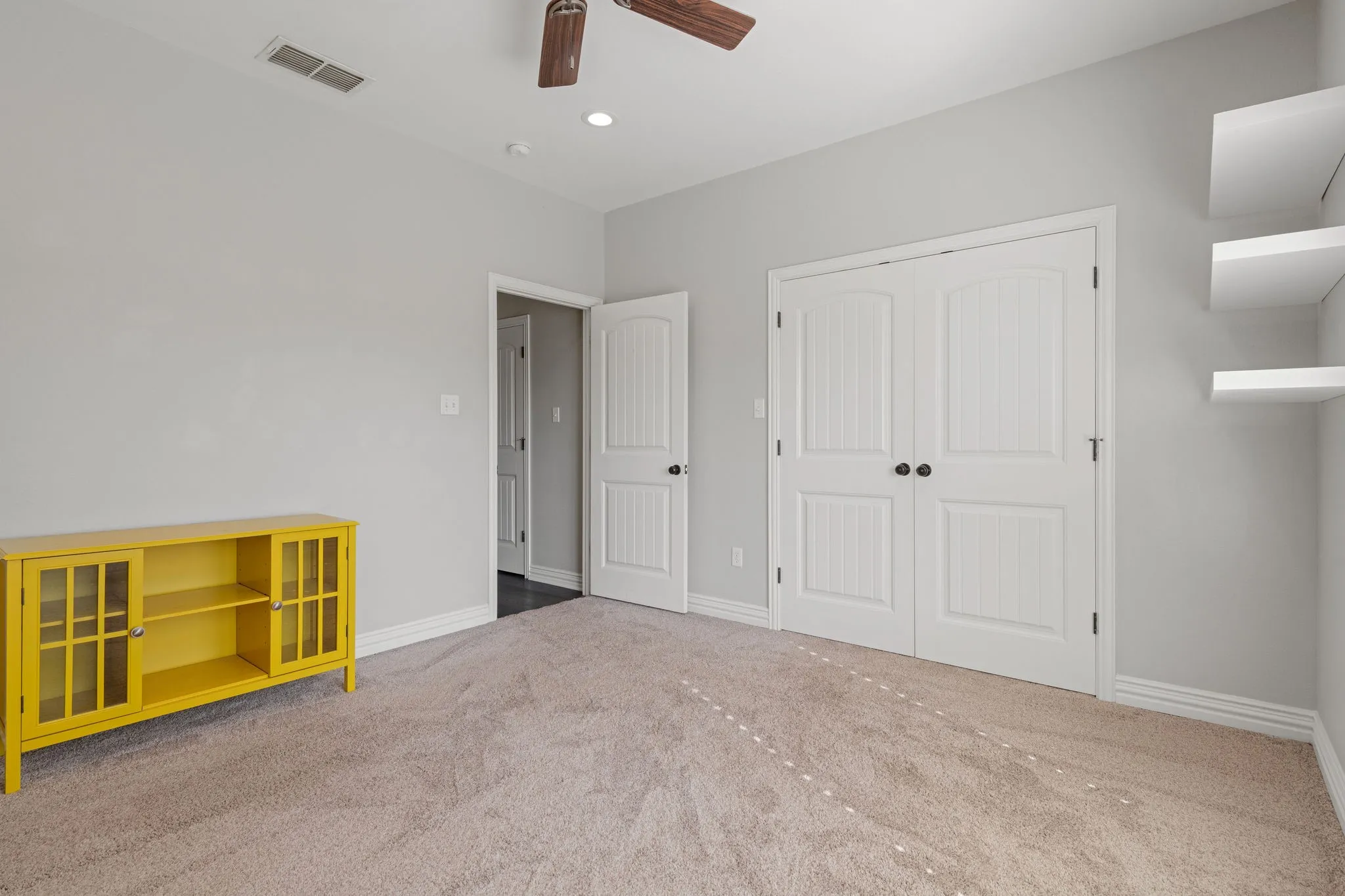 Plush carpet flooring, recessed lighting, and a ceiling fan.  Free floating shelving.