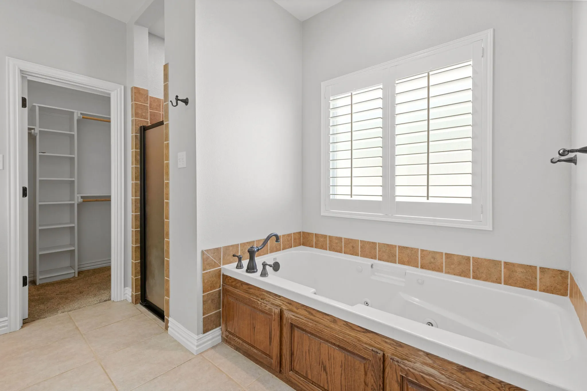 Soaking jet tub with bronze-finish fixtures, wood-finish paneling, and a tiled surround.  Wood plank shutters.  Walk in shower.  Two walk in closets.