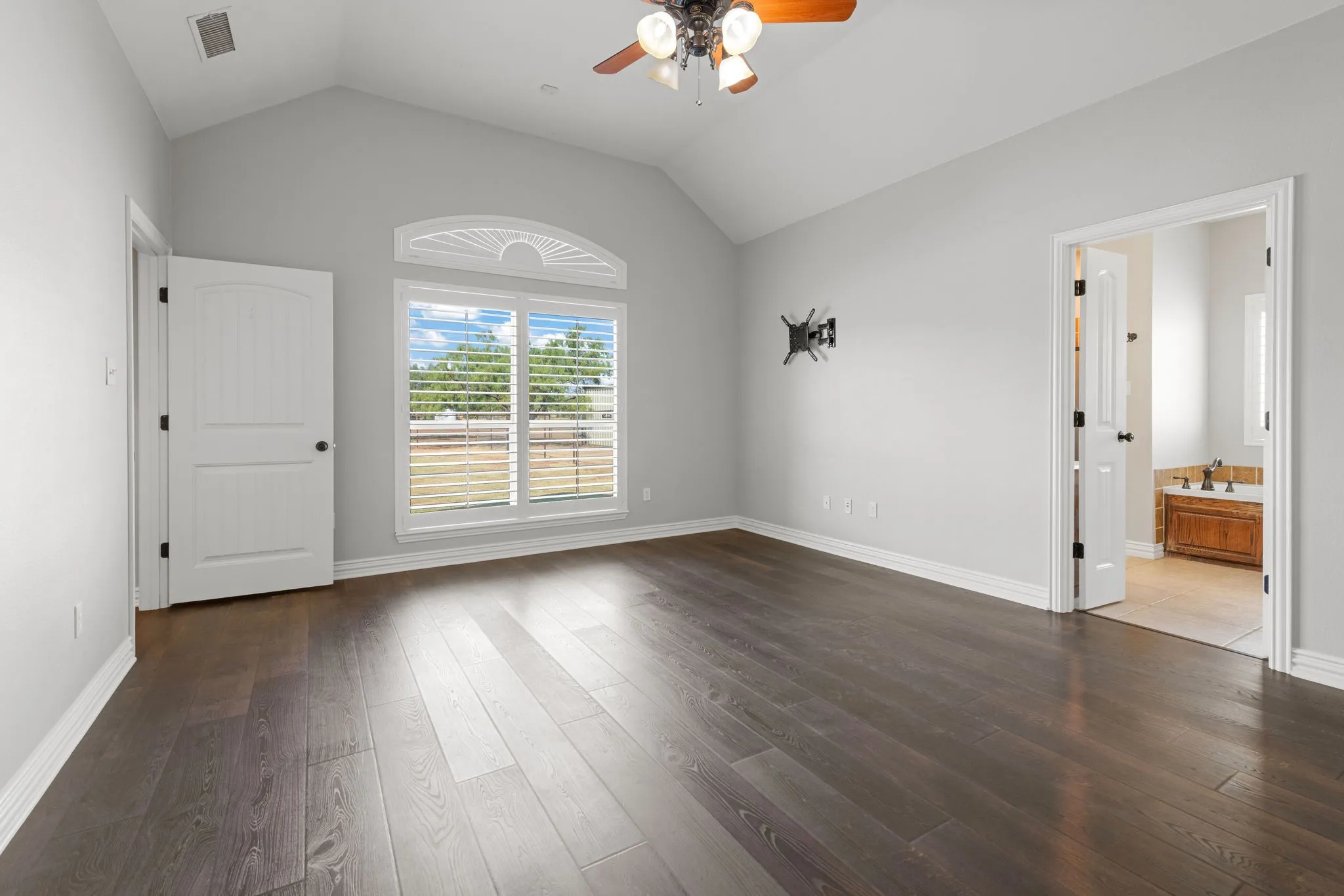Vaulted ceilings, wood-finish LVP flooring, a decorative arched window, and a ceiling fan.  Ensuite bath.