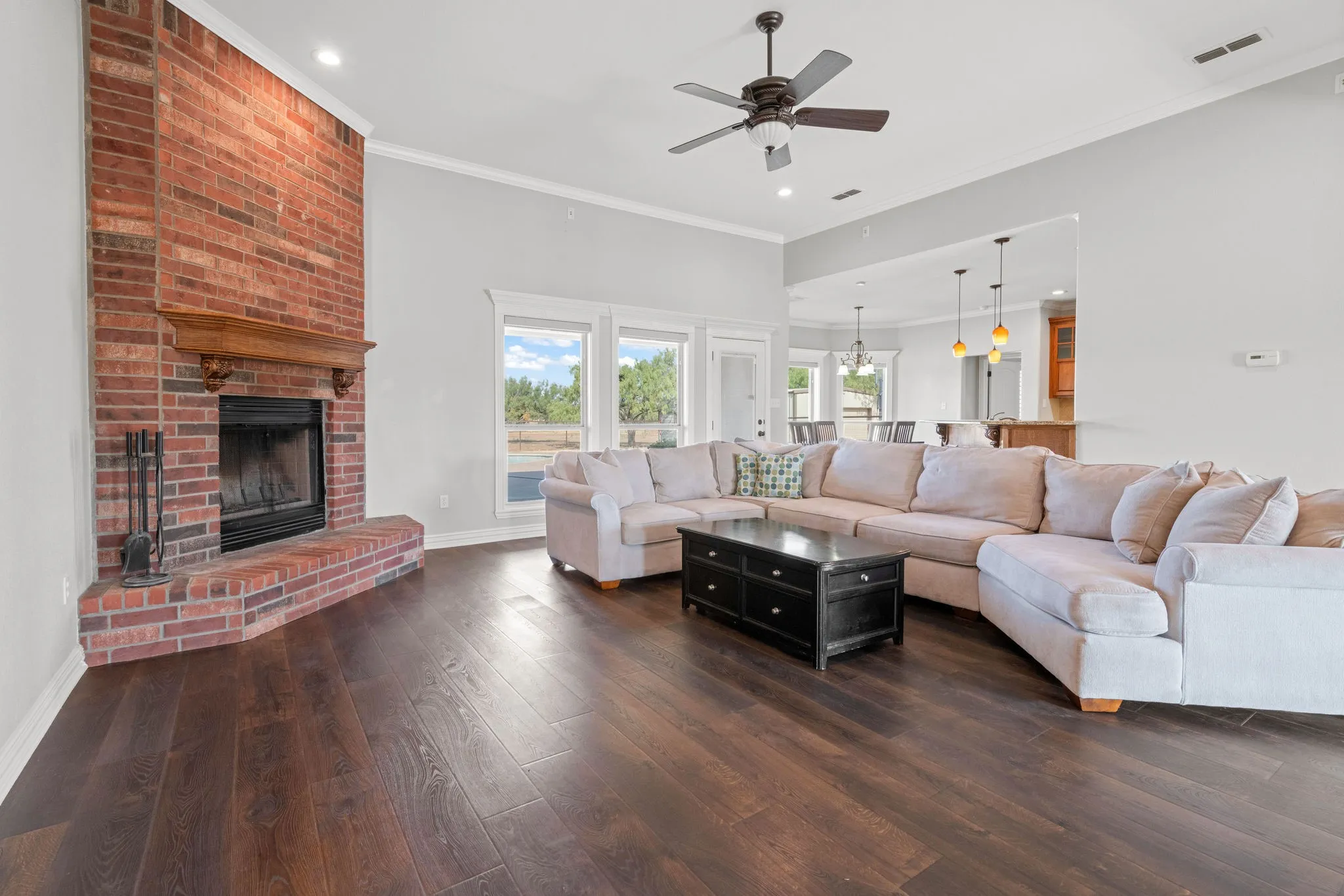 Brick fireplace with a wood mantel, recessed lighting, and a ceiling fan in the spacious living room.