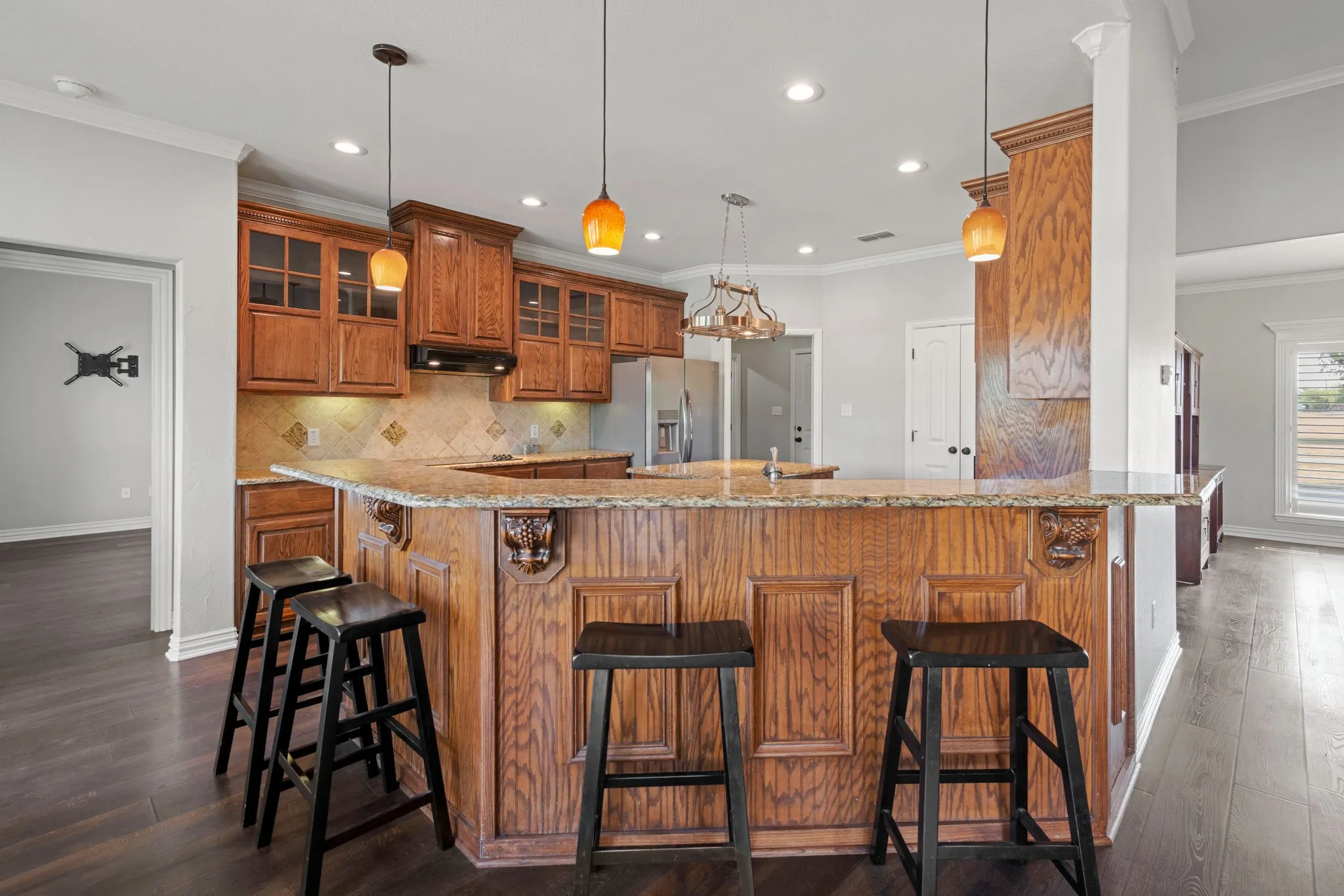 Wrap around breakfast bar. Kitchen featuring wood cabinetry, granite-finish countertops, and a tile backsplash.