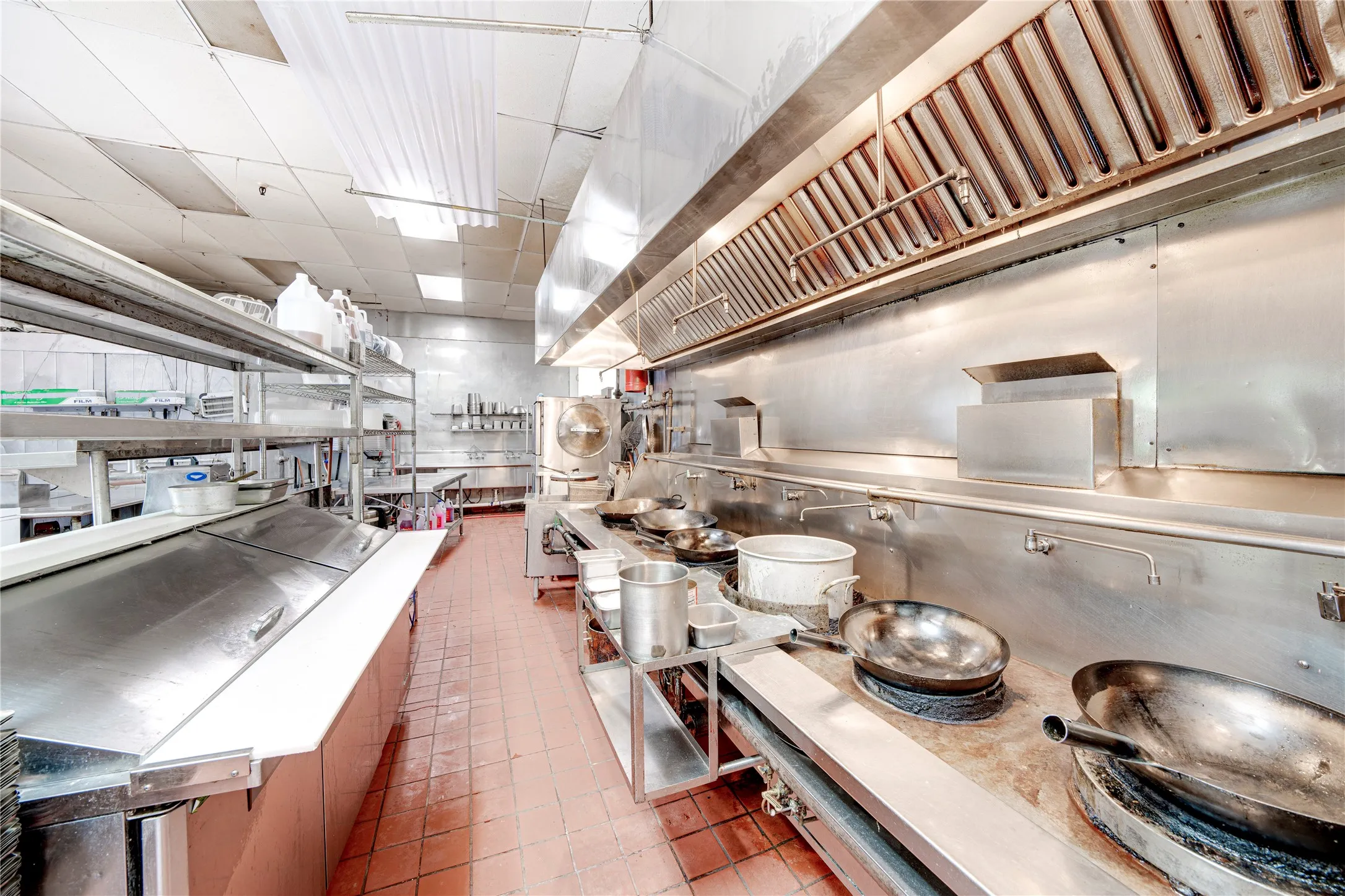 Expansive commercial kitchen with stainless steel surfaces, integrated cooking stations, and extensive overhead ventilation