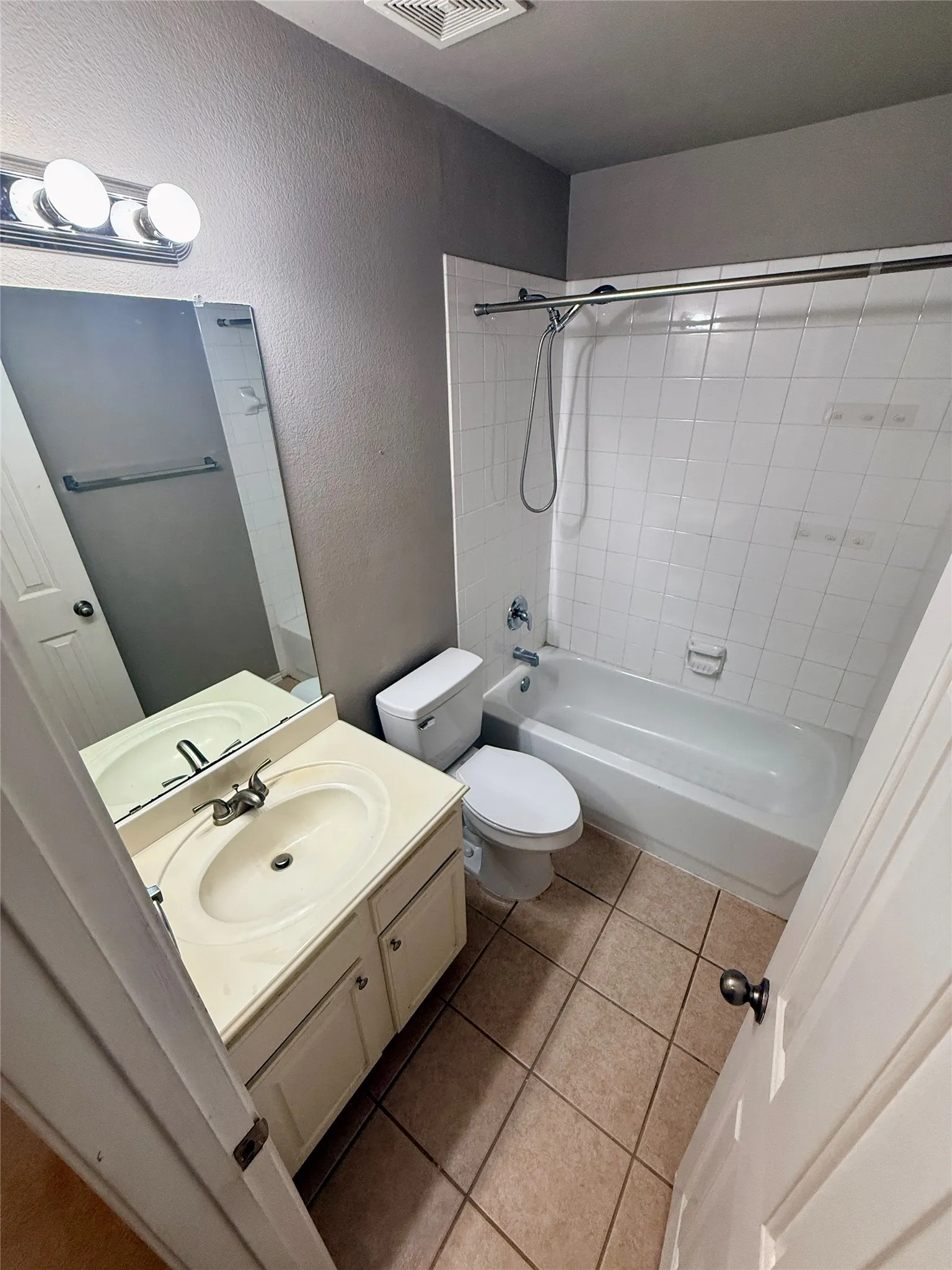 Vanity with integrated sink, white cabinetry, chrome faucet, wall-mounted mirror, and tile flooring