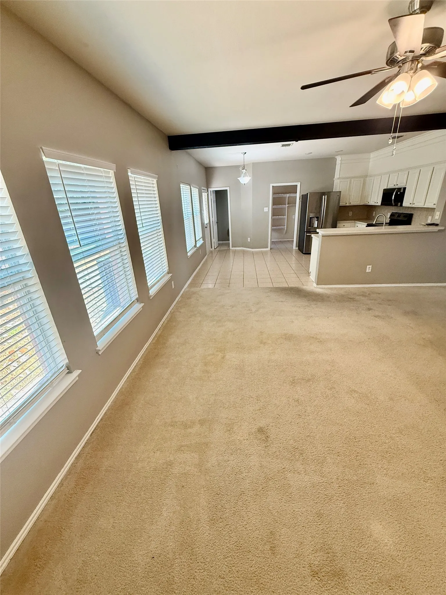 Vaulted ceiling with an exposed beam, ceiling fan, and multiple windows