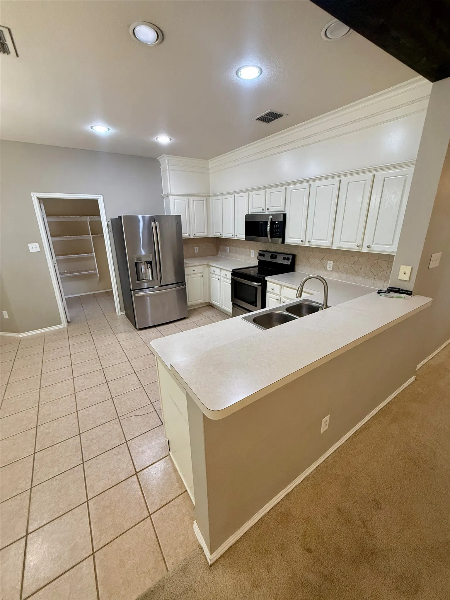 Kitchen featuring white cabinetry, stainless steel appliances, a double basin sink, and tile flooring