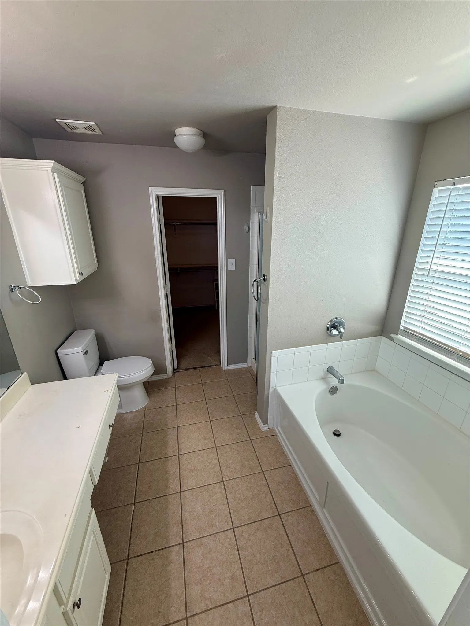 Bathroom featuring a built-in tub, separate shower, vanity with integrated sink, toilet, and tile flooring