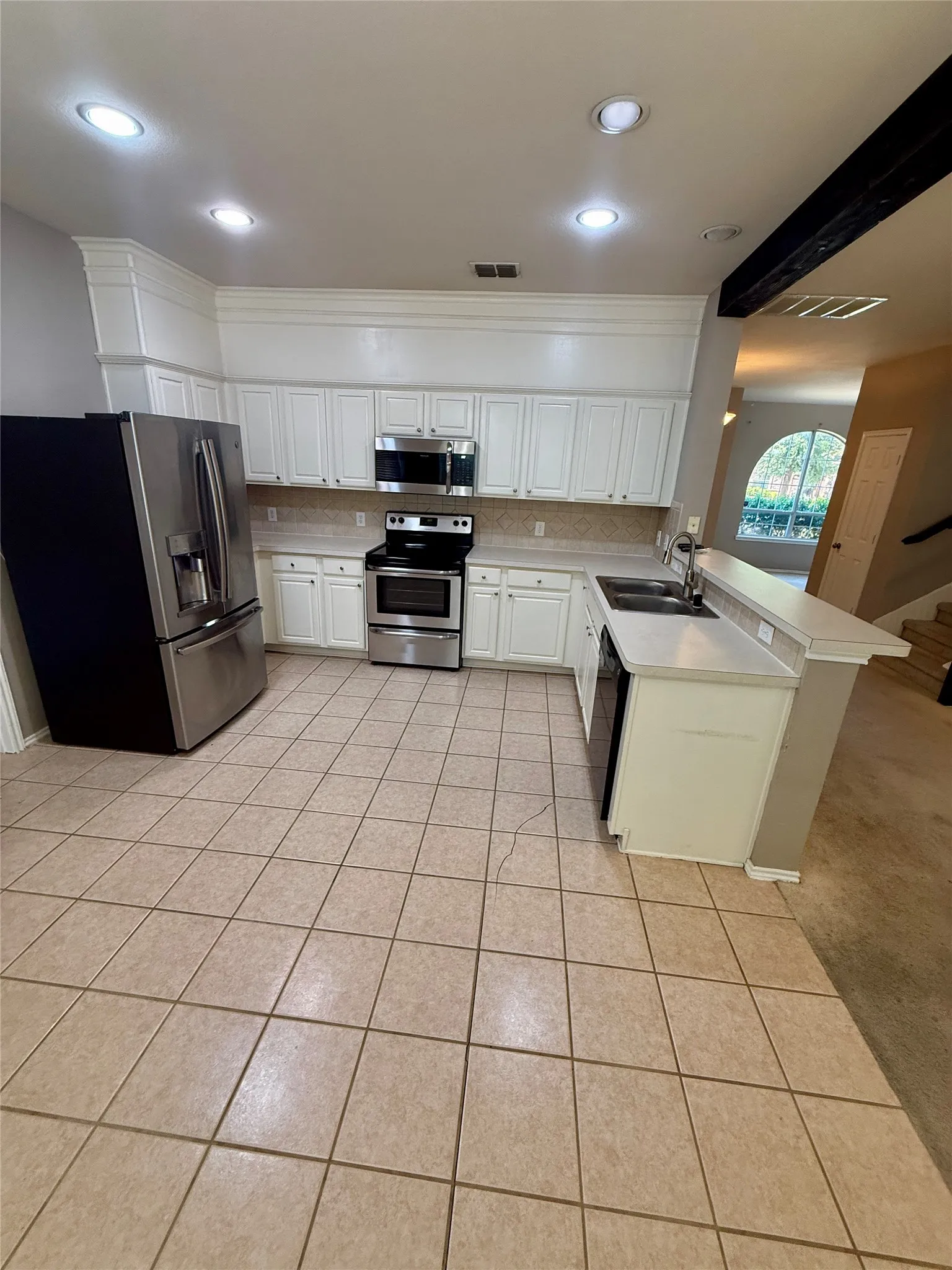 Kitchen featuring white cabinetry, stainless steel appliances, recessed lighting, tile flooring, and a breakfast bar with a sink