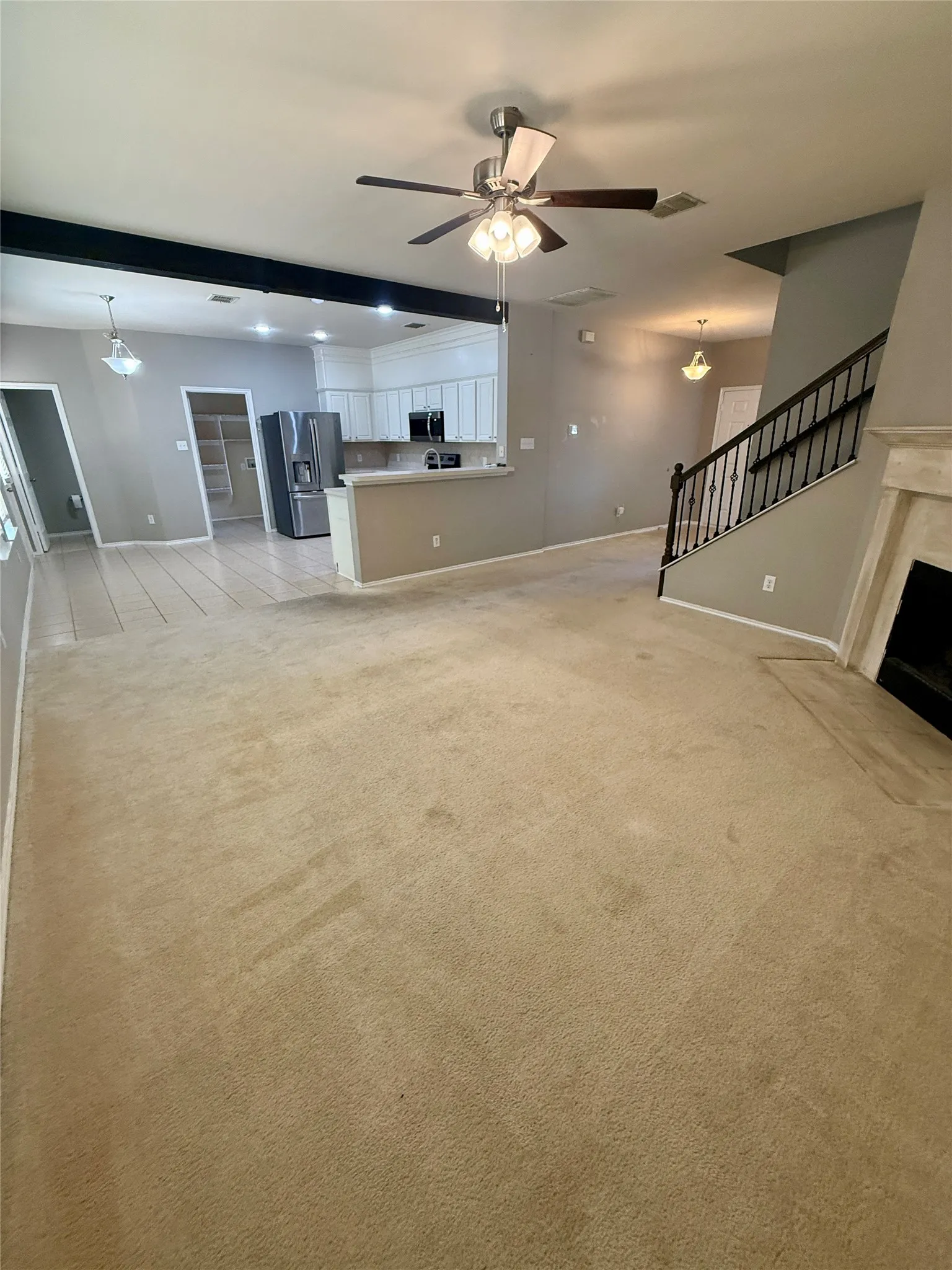 Spacious living area with carpet flooring, a ceiling fan, and a fireplace with a mantel