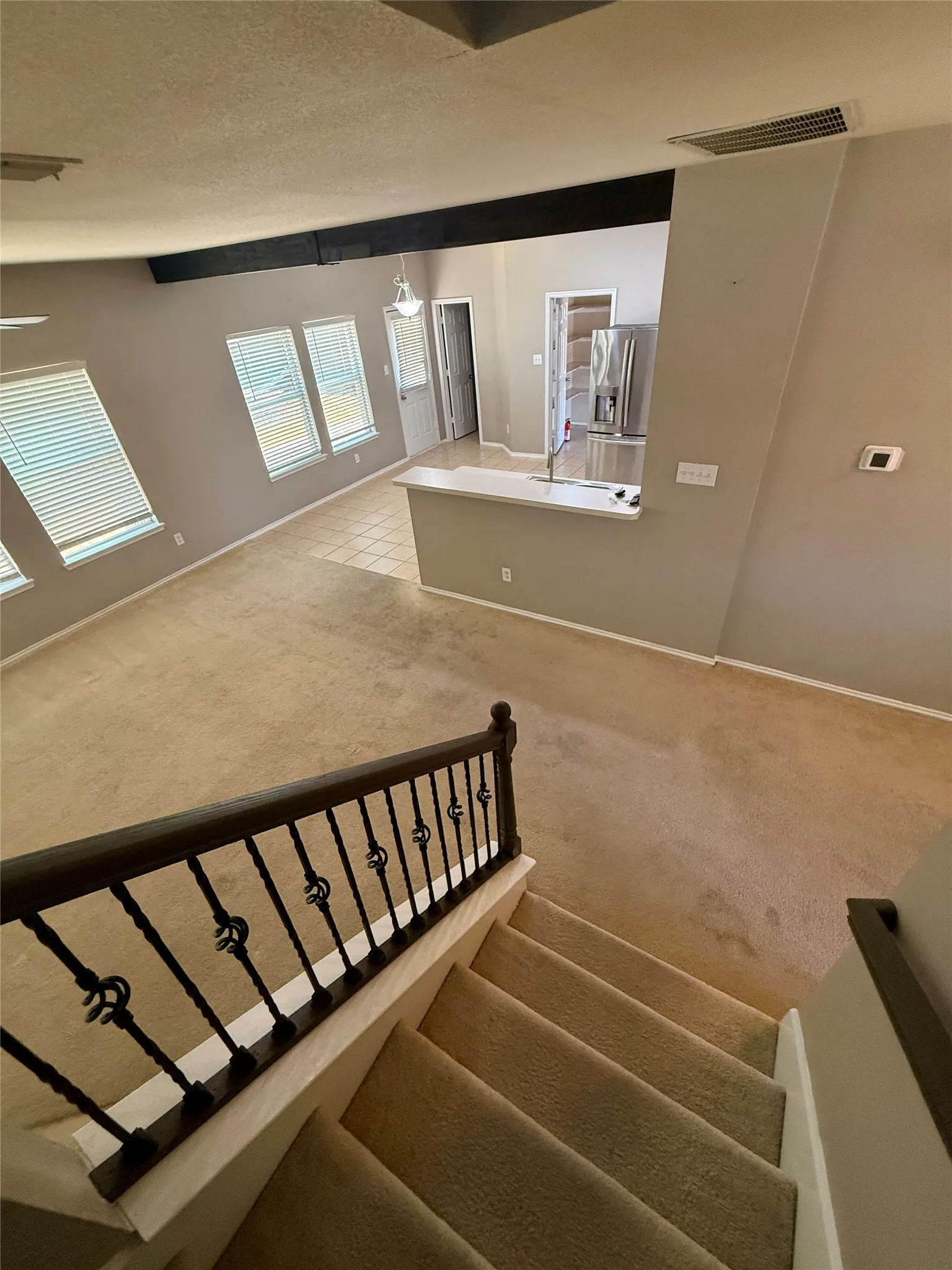 Vaulted ceiling featuring a dark wood-finish beam, carpeted flooring, tiled flooring, an iron balustrade, and a kitchen island with a built-in sink