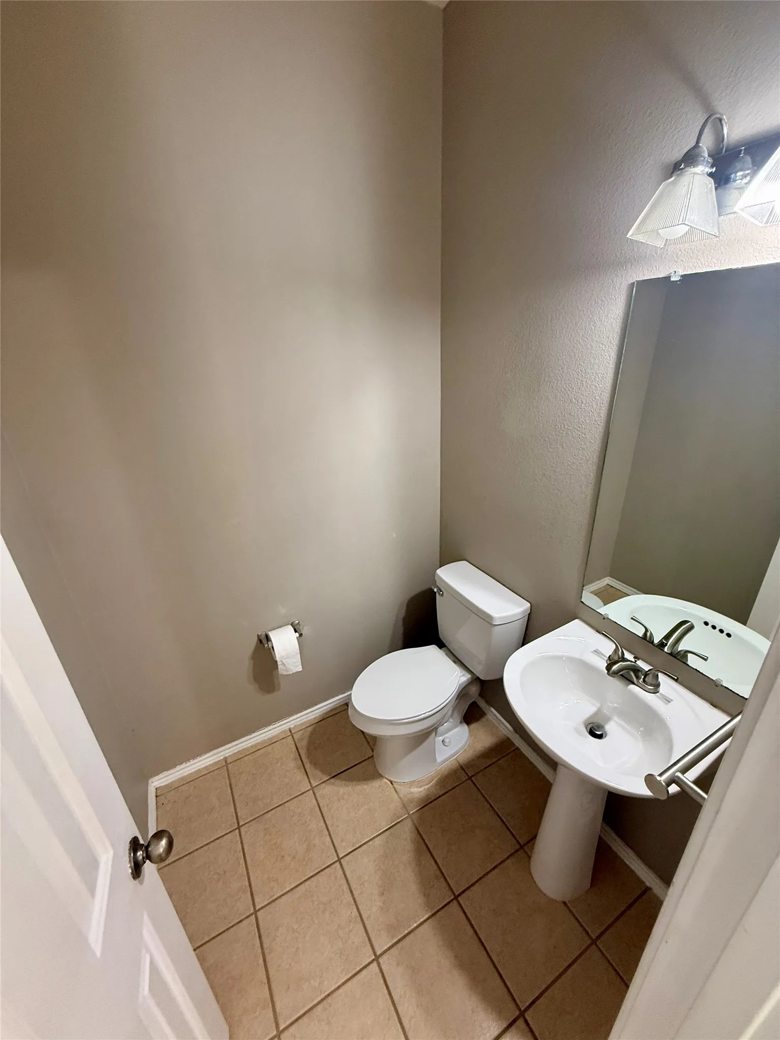 Pedestal sink with chrome faucet, wall-mounted mirror, two-light fixture, white toilet, and tile flooring