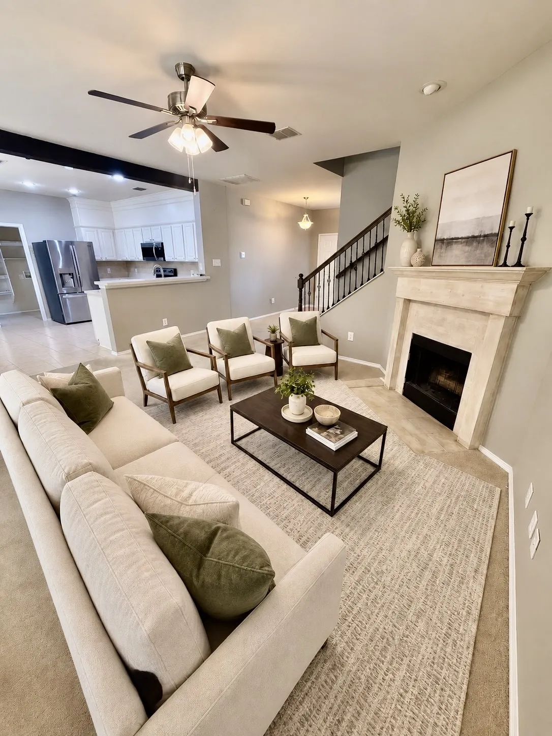 Living space featuring a natural stone fireplace, wood-finish ceiling fan, and open concept to the kitchen with white cabinetry and stainless-steel appliances