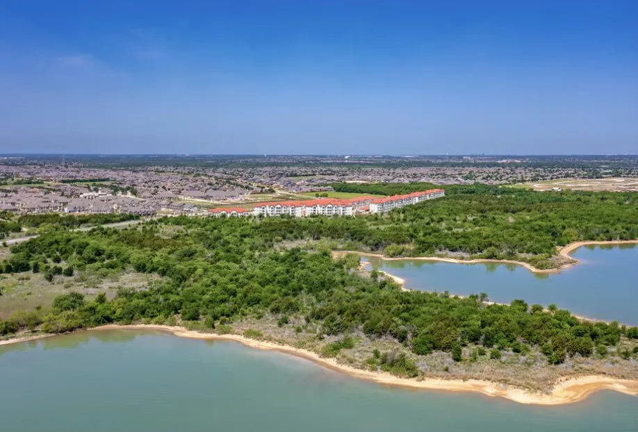 Expansive natural landscape featuring a prominent body of water, dense tree coverage, and distant residential structures