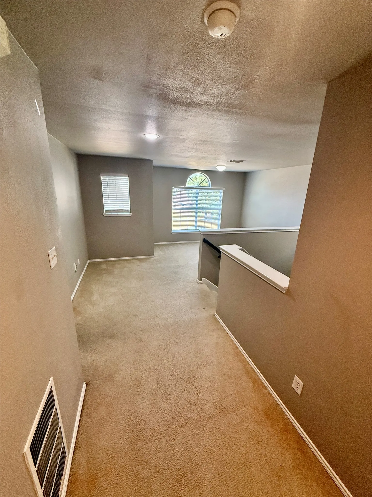 Carpeted secondary living space featuring multiple windows, recessed lighting, and a white balustrade