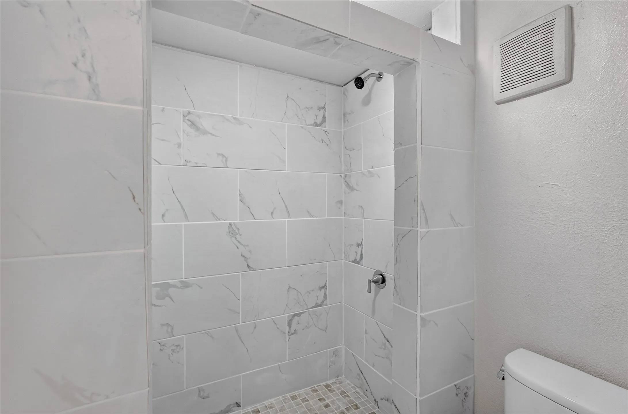 Shower enclosure with large format tile walls, recessed shower niche, rain shower head, and mosaic tile floor