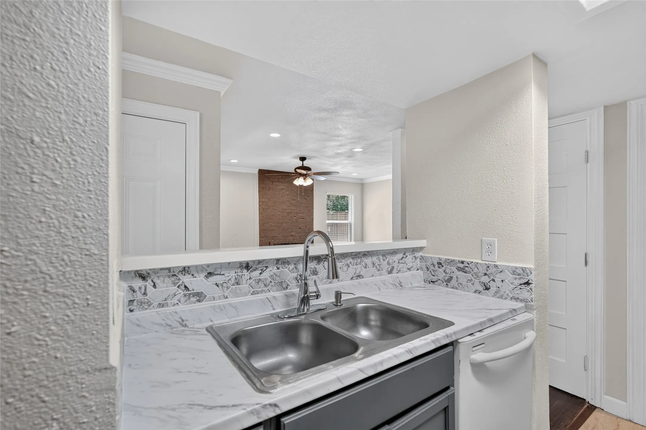 Modern kitchen and bath featuring a stainless steel double-basin sink with pull-down faucet, engineered stone countertops with veining detail, and a coordinating tile backsplash