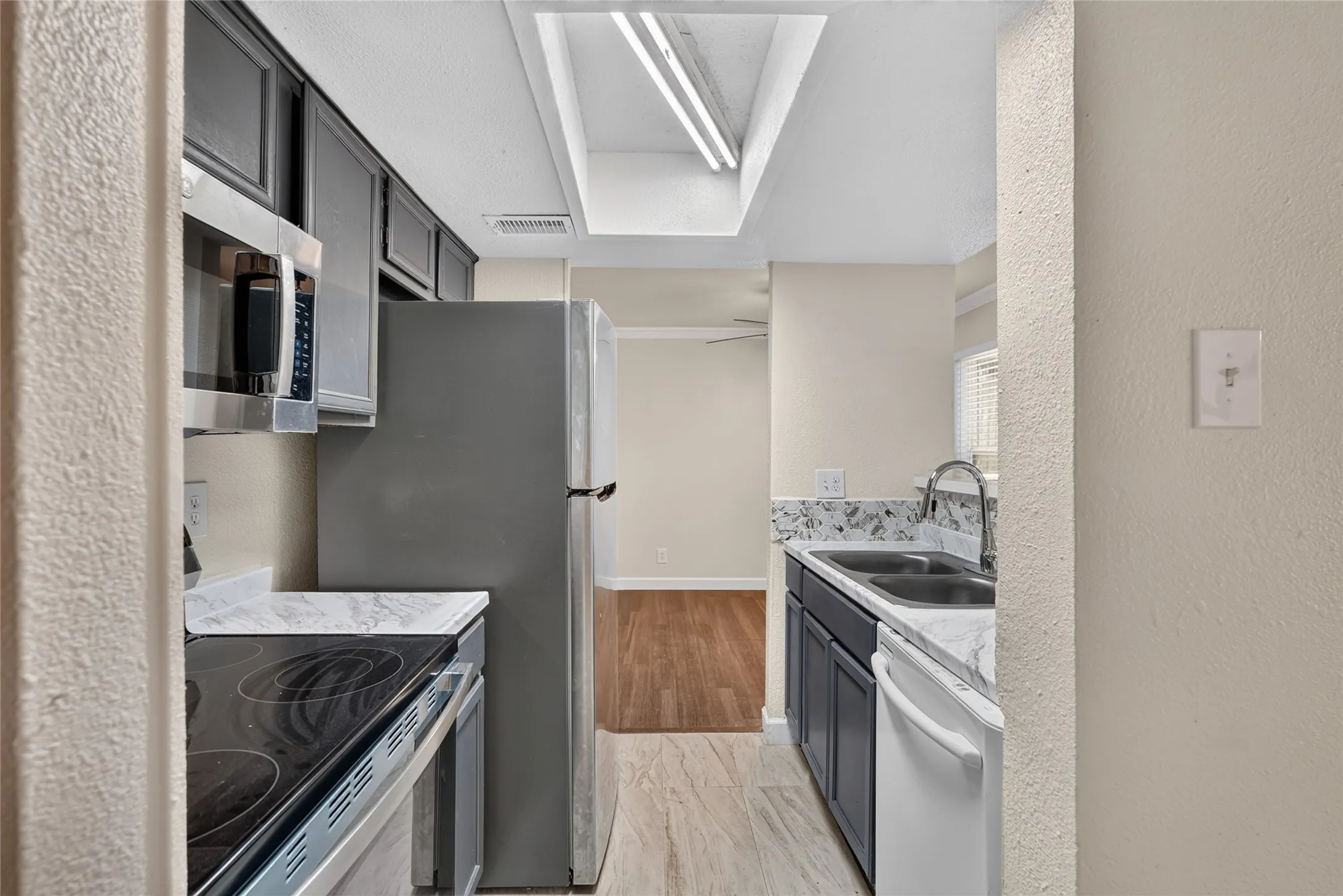Galley kitchen featuring dark cabinetry, stainless steel appliances, stone-look countertops, and recessed lighting