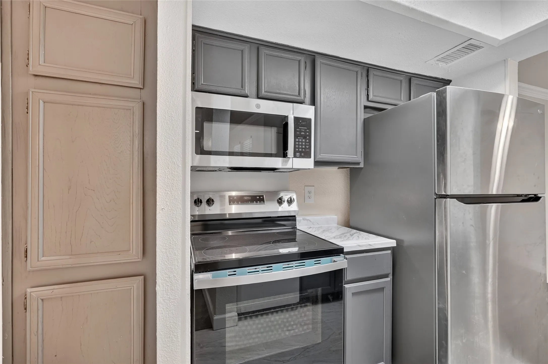 Stainless steel appliances, built-in microwave, dark gray cabinetry, light countertops, paneled storage cabinet