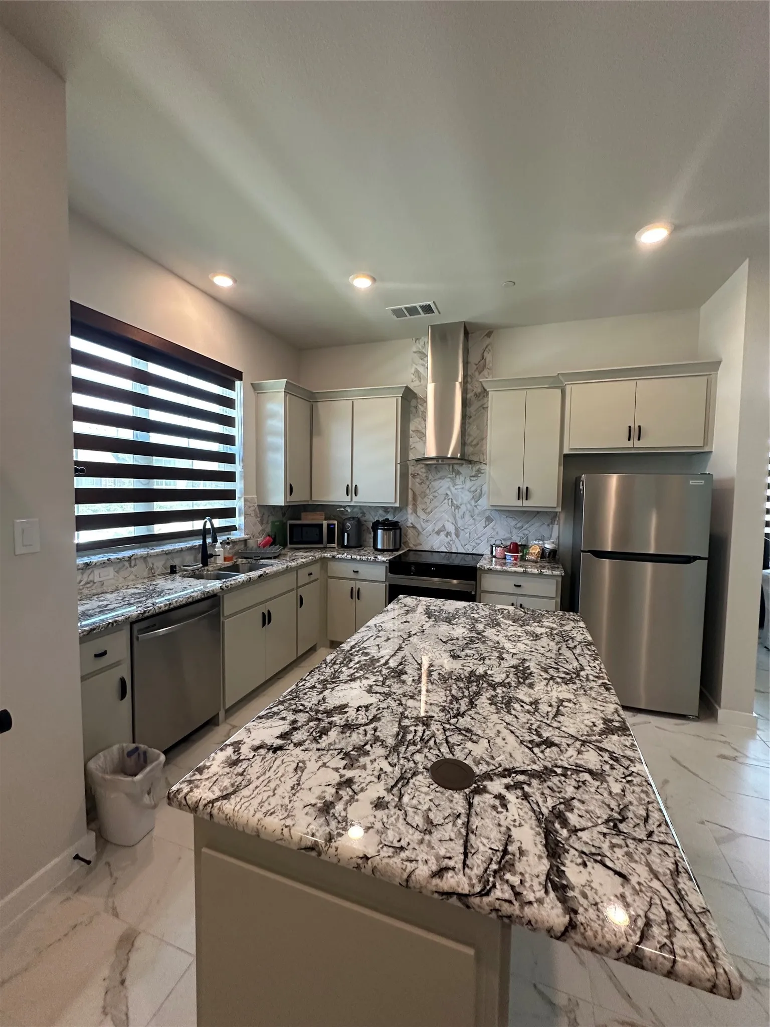 Spacious kitchen featuring an expansive island with a polished countertop, stainless steel appliances, upper and lower cabinetry, recessed lighting, and a coordinating backsplash