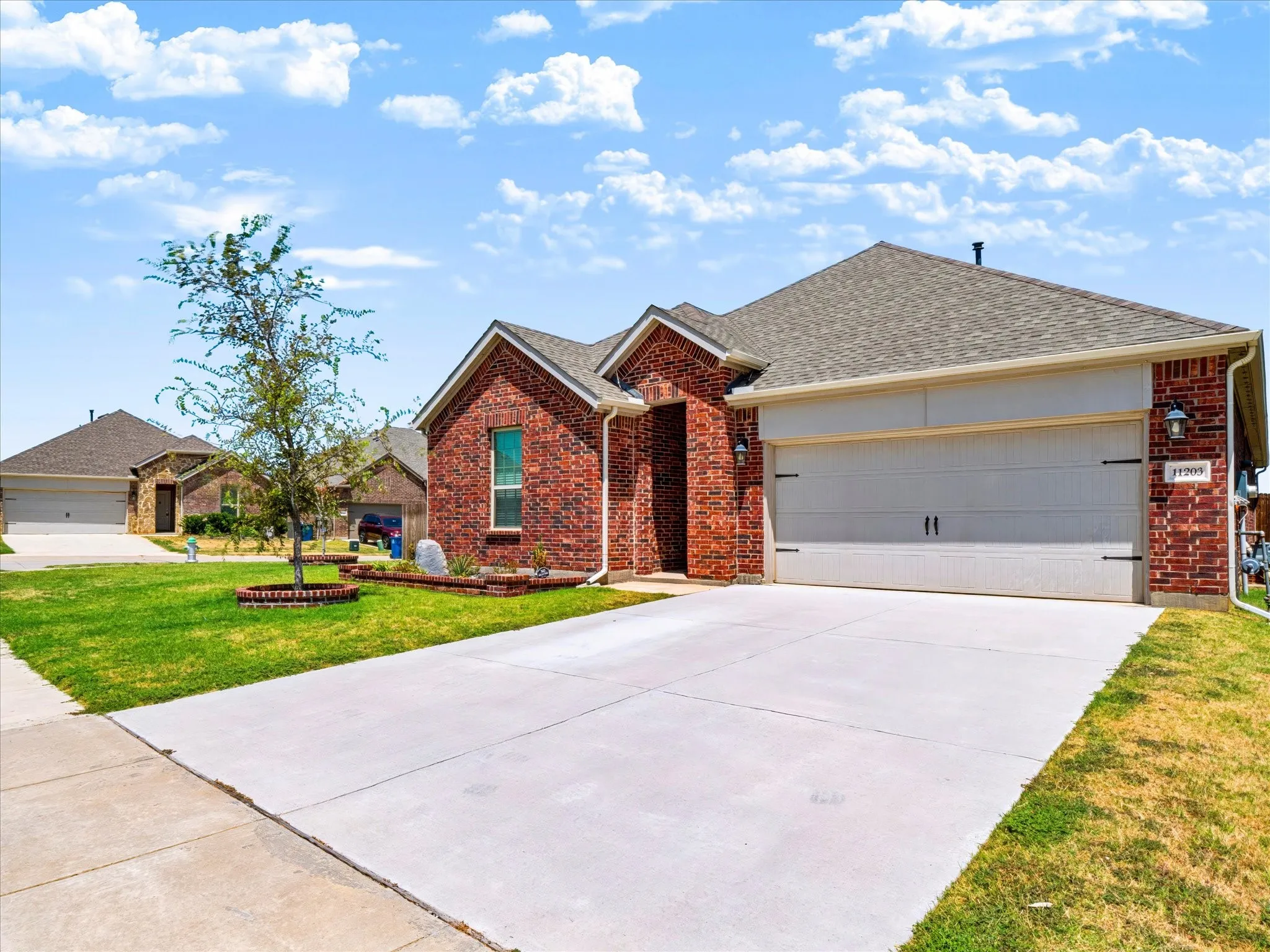 Brick exterior, attached two-car garage, concrete driveway, front yard landscaping, and a pitched shingle roof