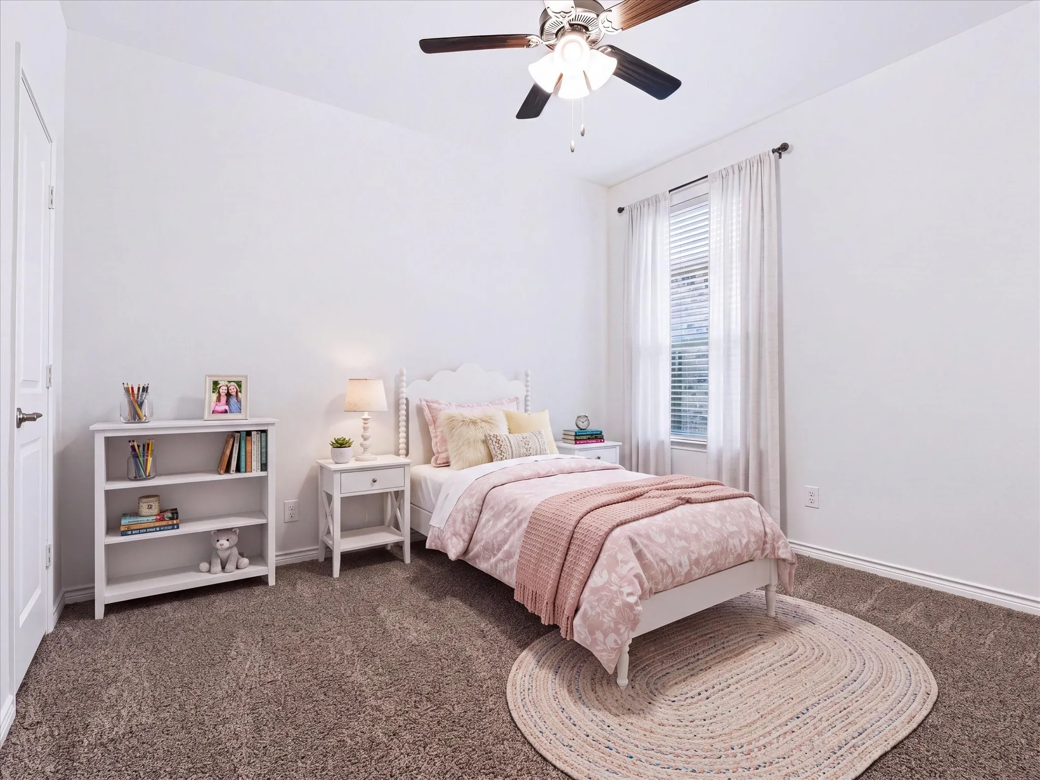 Plush carpet flooring, ceiling fan with integrated lighting, window with blinds and sheer curtains, and a solid white door with dark hardware