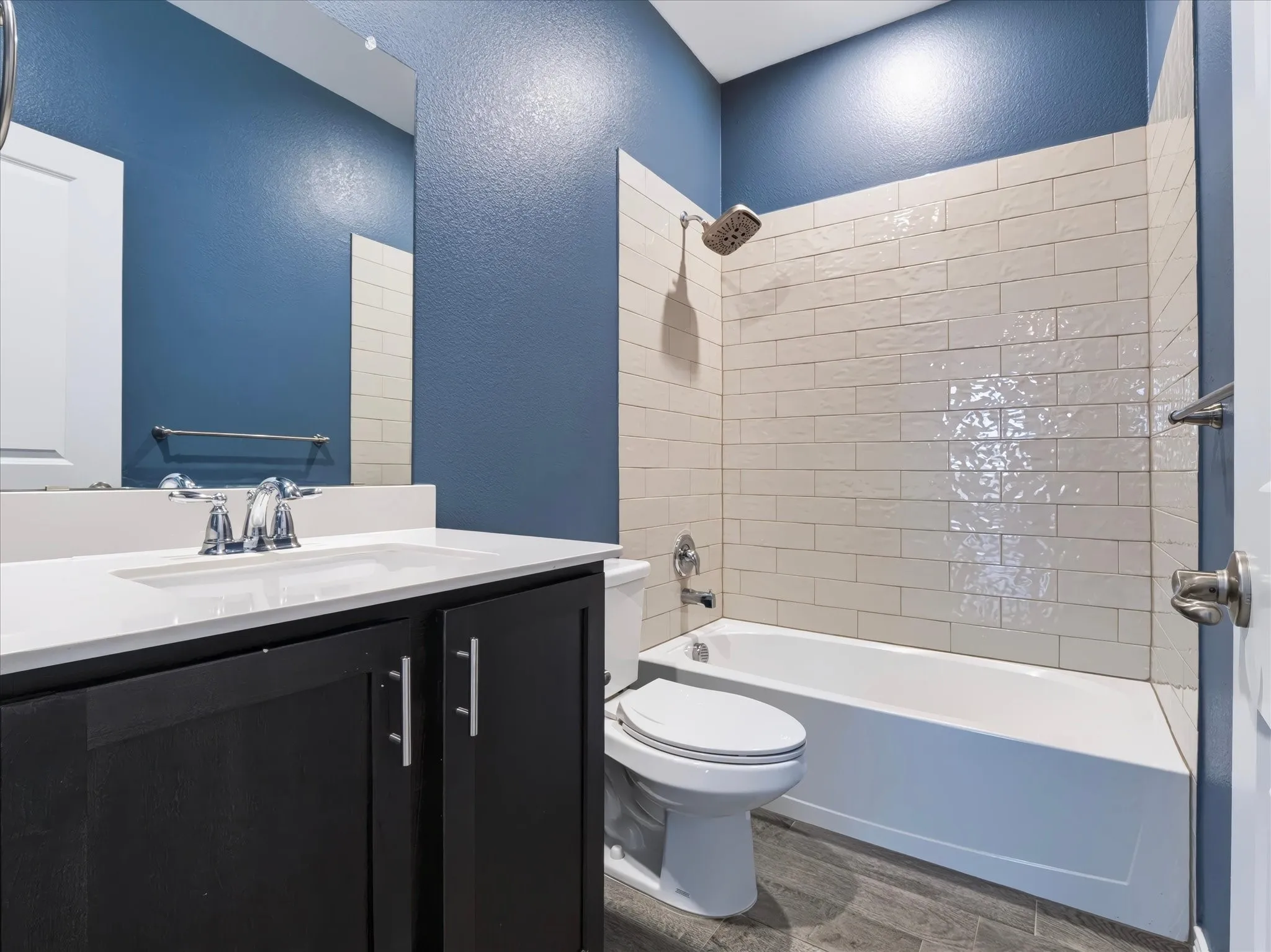 Modern bathroom featuring a black vanity with white countertop and rectangular sink, subway tile surround in the tub/shower area, brushed nickel fixtures, and a fresh blue accent wall with recessed lighting throughout