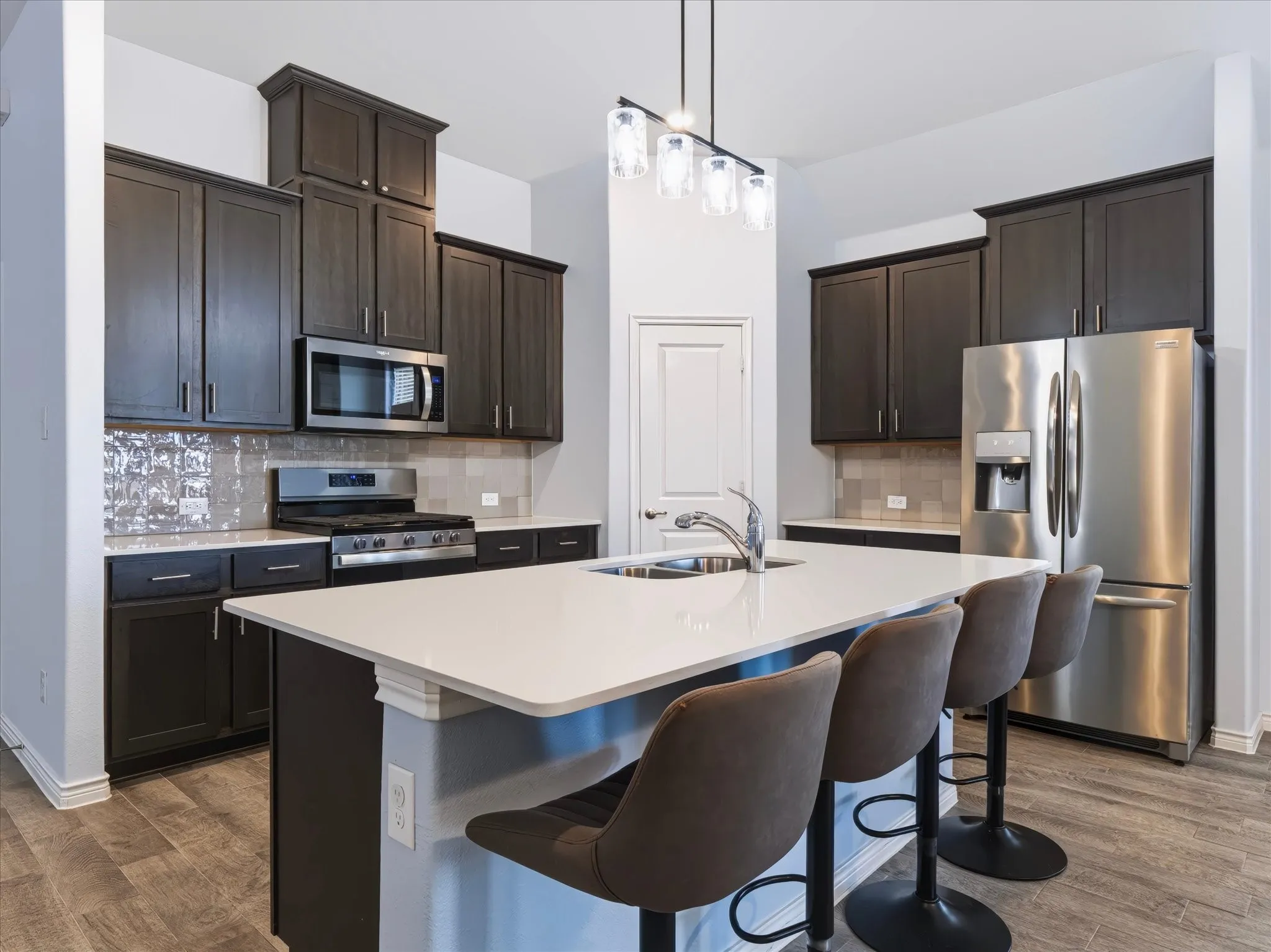 Kitchen featuring dark wood-finish cabinetry, stainless steel appliances, a white countertop island with an integrated sink, and wood-finish flooring
