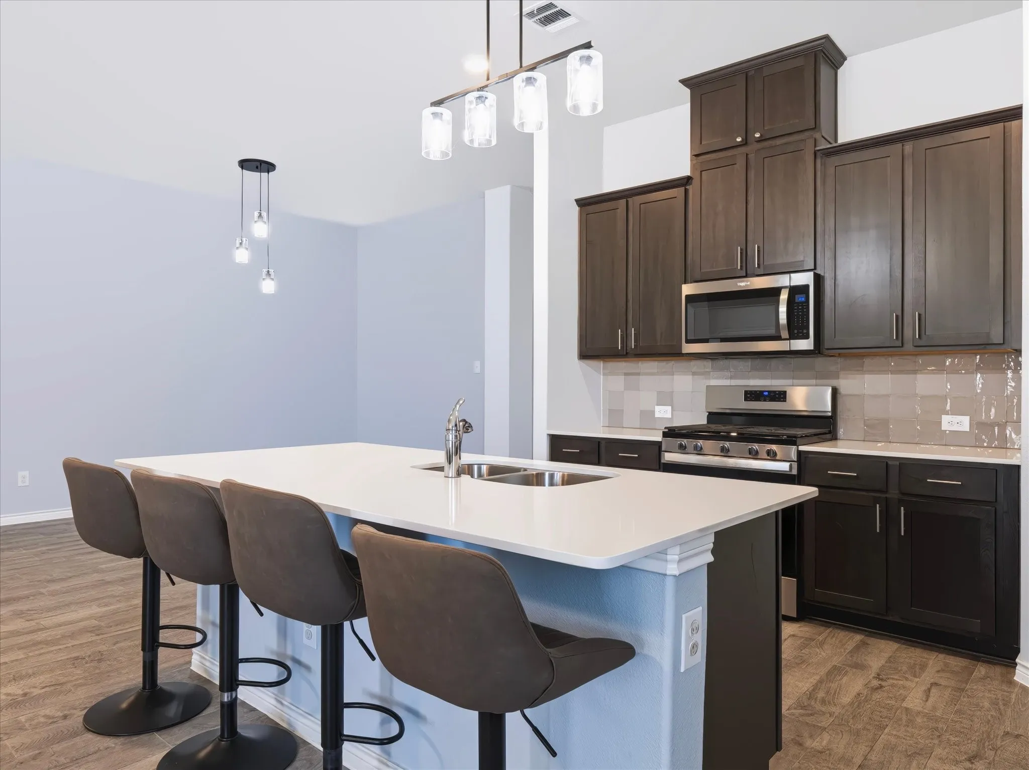 Kitchen featuring dark wood-finish cabinetry, stainless steel appliances, a tile backsplash, and a large island with an integrated double sink and modern pendant lighting