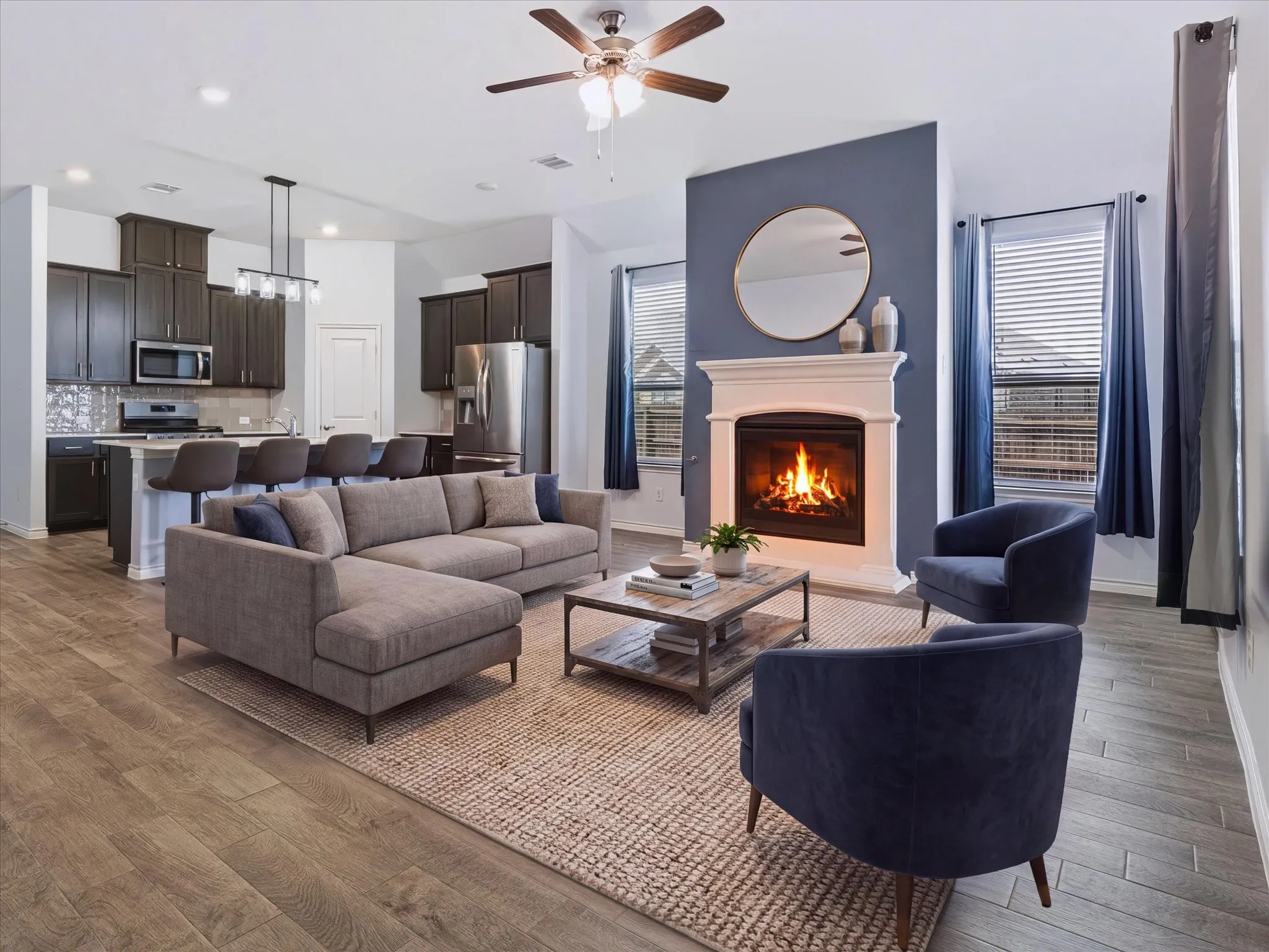 Open-concept living space featuring wood-finish flooring, a ceiling fan, and a fireplace with a white mantel