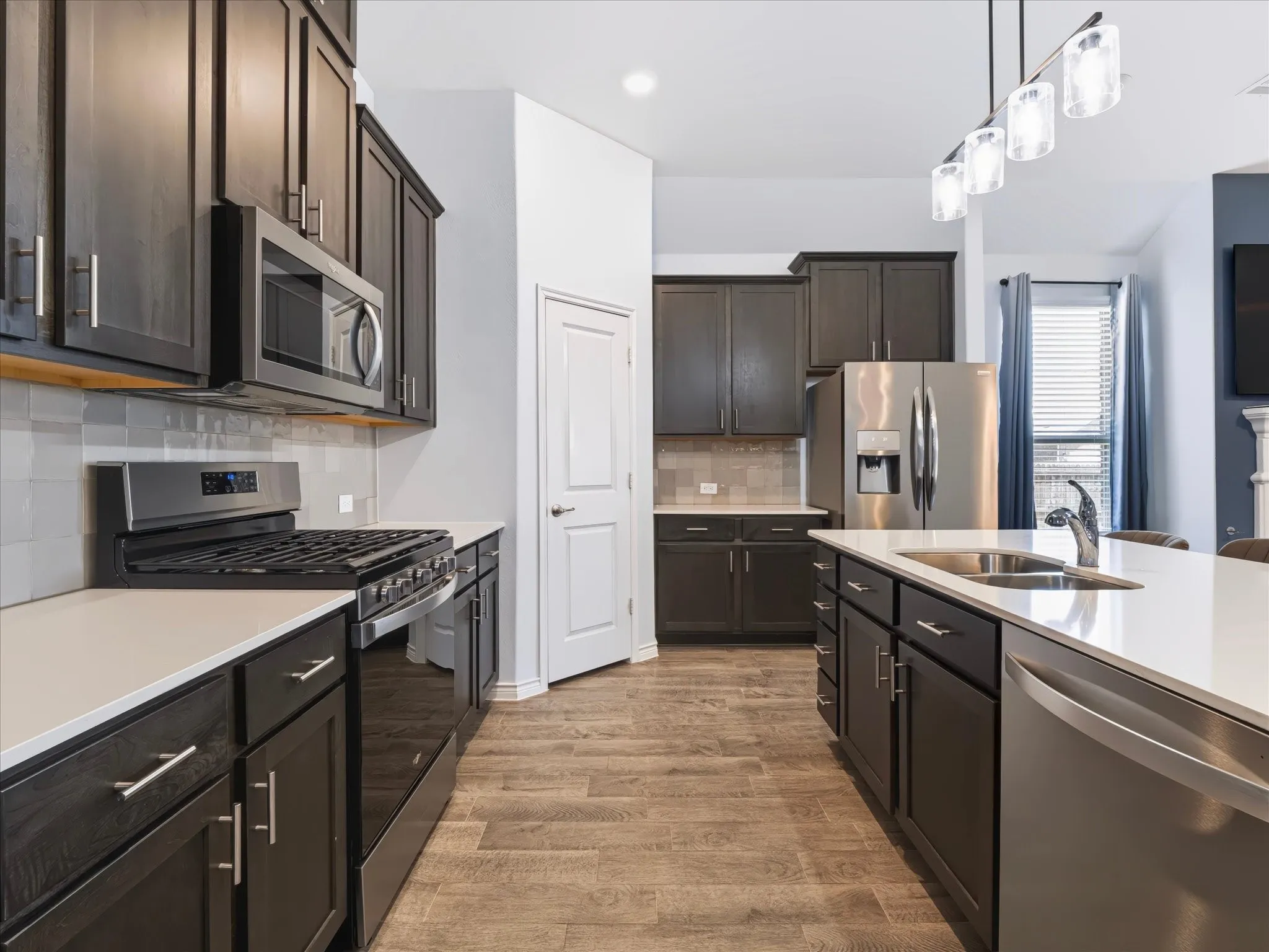 Contemporary kitchen featuring dark wood-finish cabinetry, stainless steel appliances, a center island with sink, and wood-finish flooring