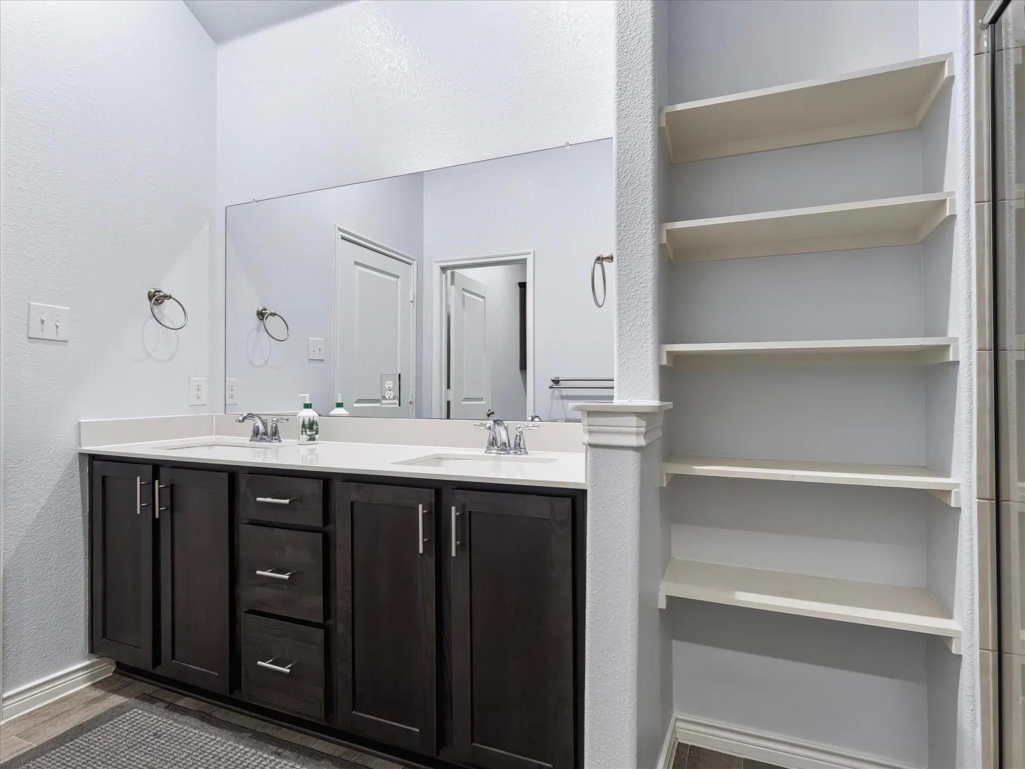 Dual vanity with dark wood-finish cabinetry, chrome hardware, and a single large mirror