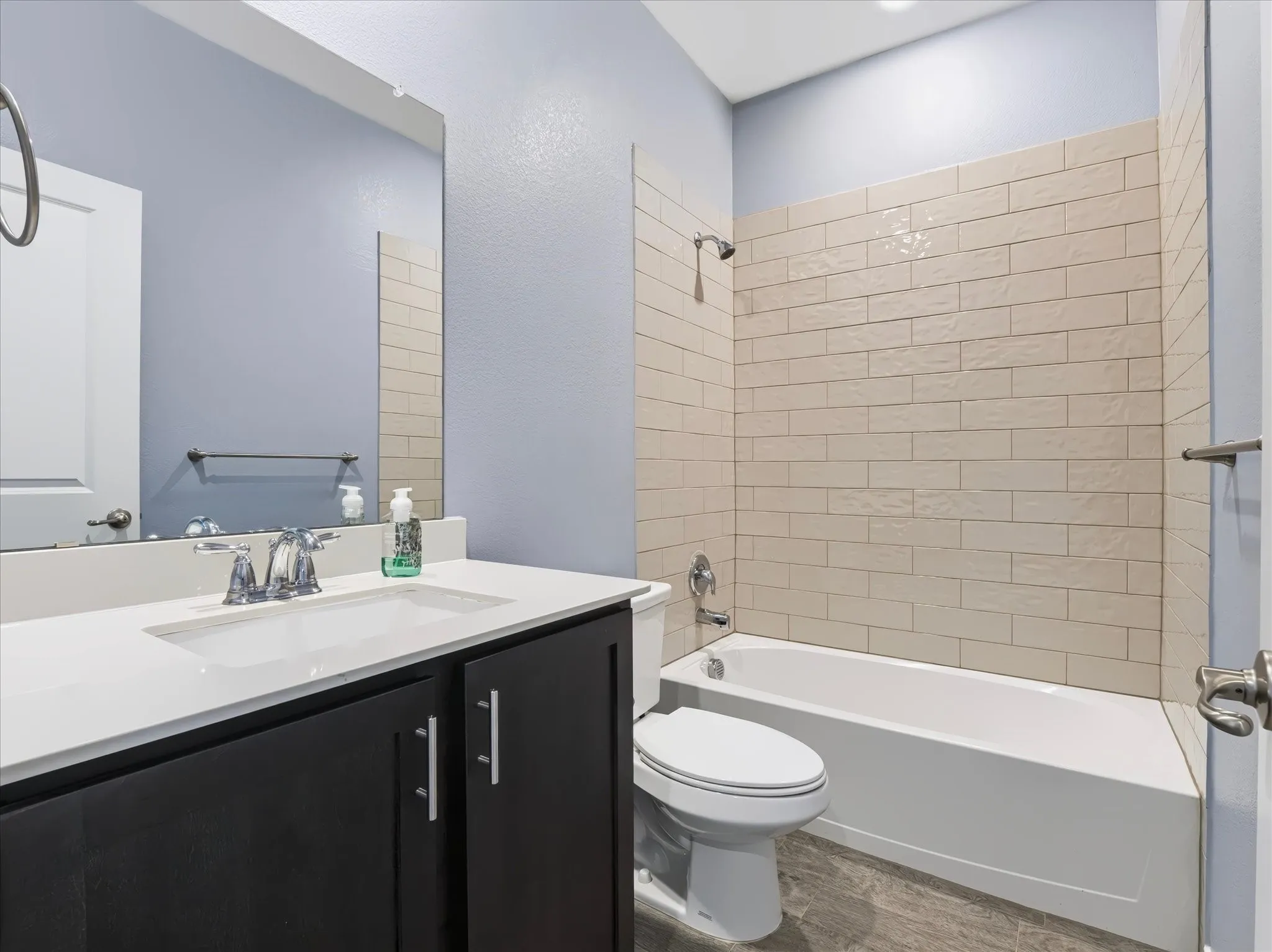Bathroom featuring a white bathtub, subway tile surround, dark wood-finish vanity, white countertop, and large wall-mounted mirror