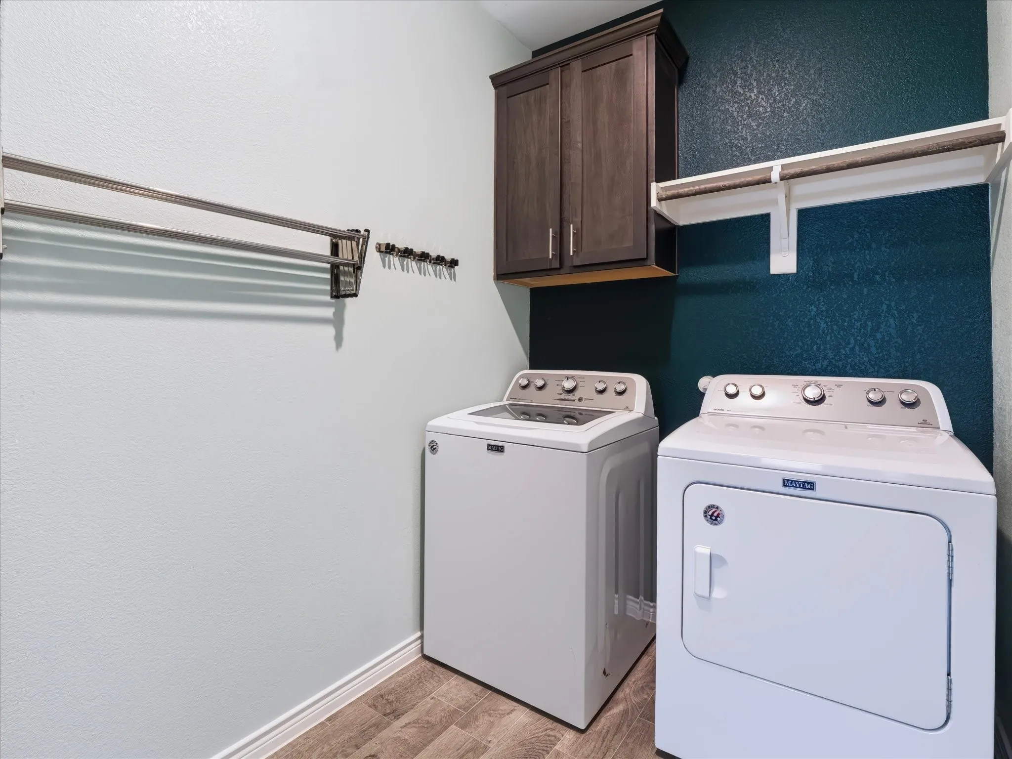 Laundry area featuring wood-finish flooring, a wall-mounted drying rack, dark wood-finish cabinetry, and a white storage shelf