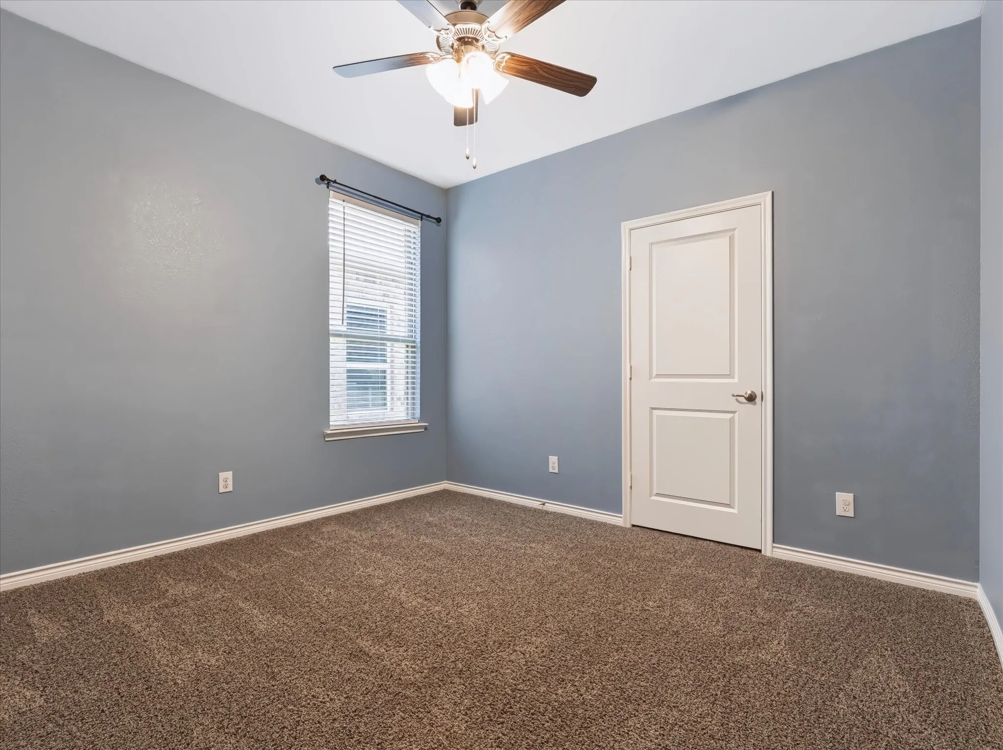 Neutral-toned carpeting, light blue wall paint, white trim, a ceiling fan with integrated lighting, and a single window with blinds