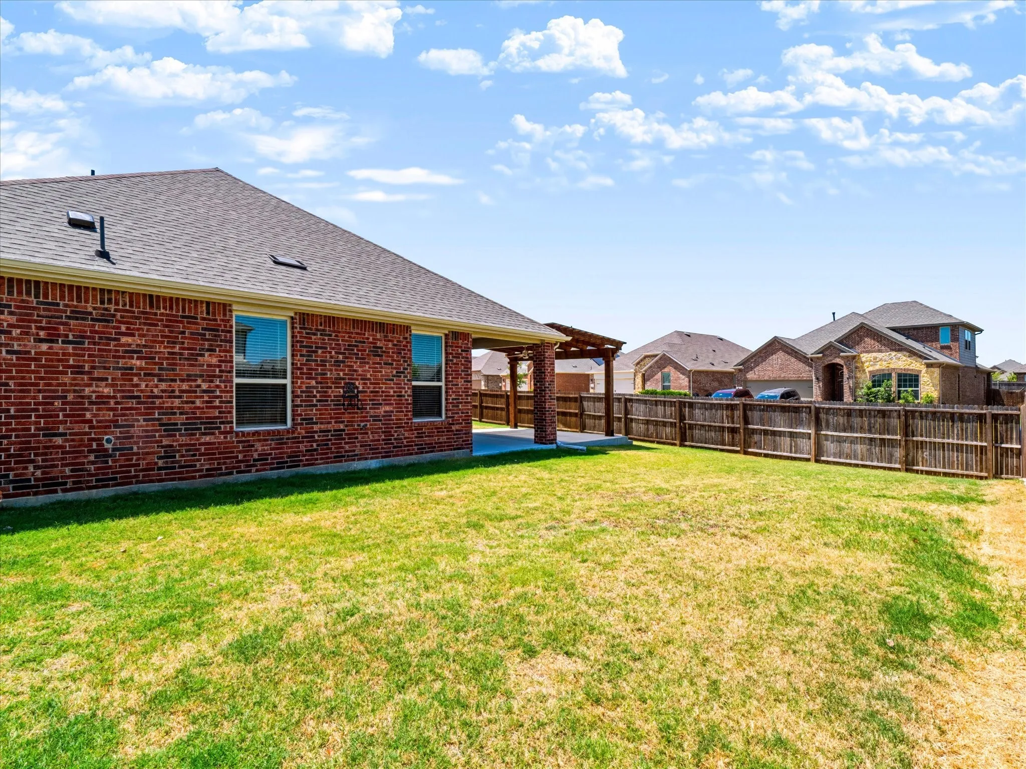 Brick exterior with multiple windows, covered patio, and a wood pergola