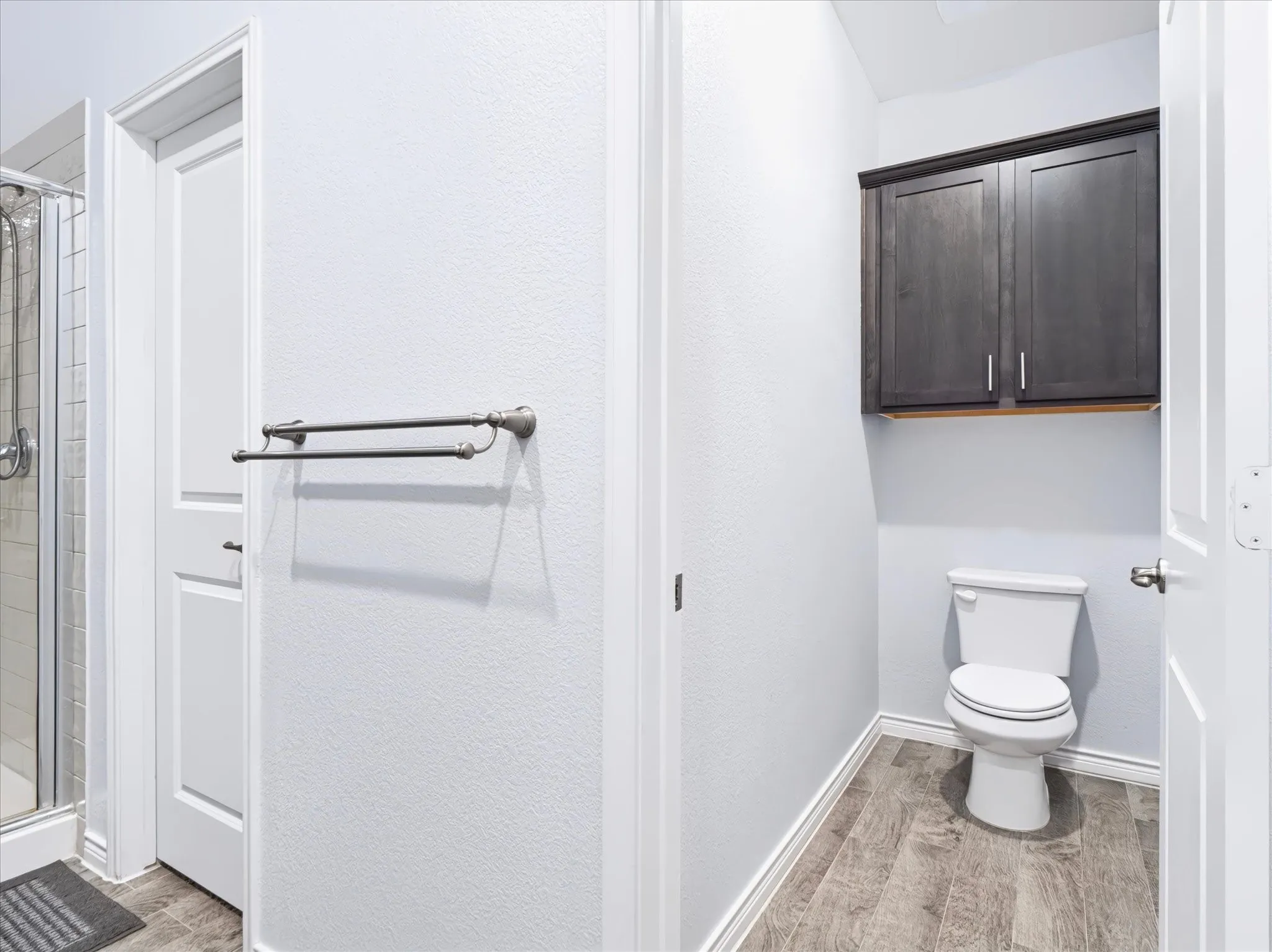 Dual vanity bathroom featuring white cabinetry, wood-finish flooring, and contemporary fixtures including a toilet and towel bar